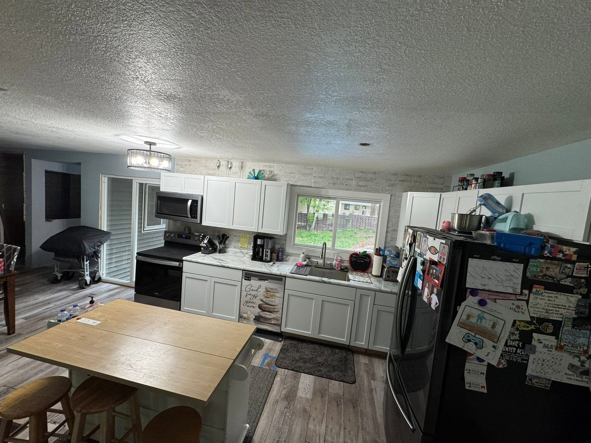 Open kitchen with white cabinets, island table, and large refrigerator covered in magnets and papers.