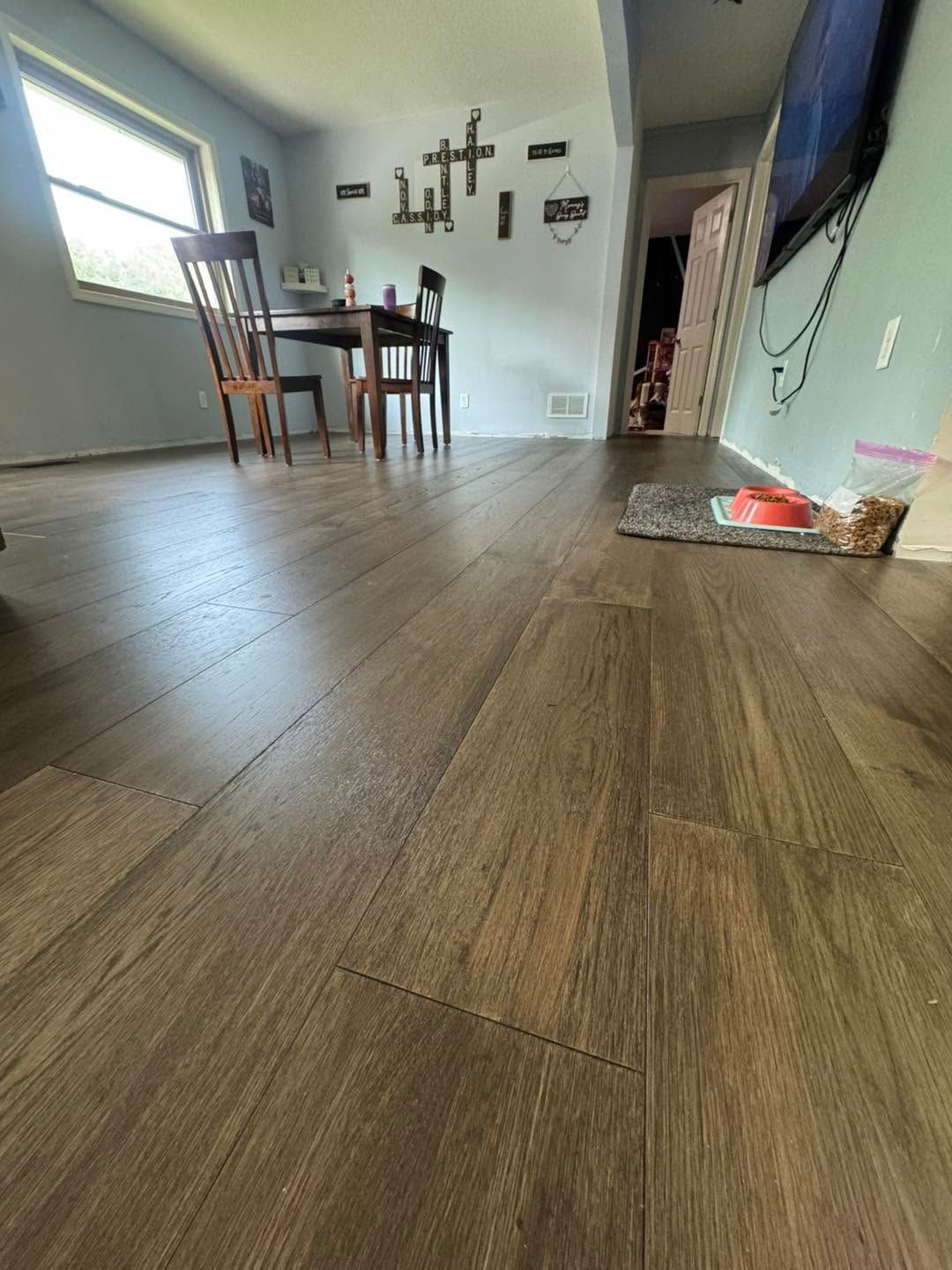 Low-angle view of a living room with wood flooring, dining table, wall decor, and a TV on the right.