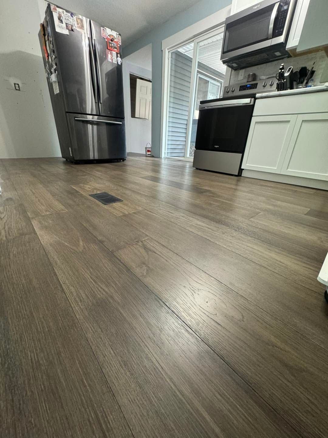 Kitchen with wood-look flooring, stainless steel refrigerator, and black oven near white cabinets.