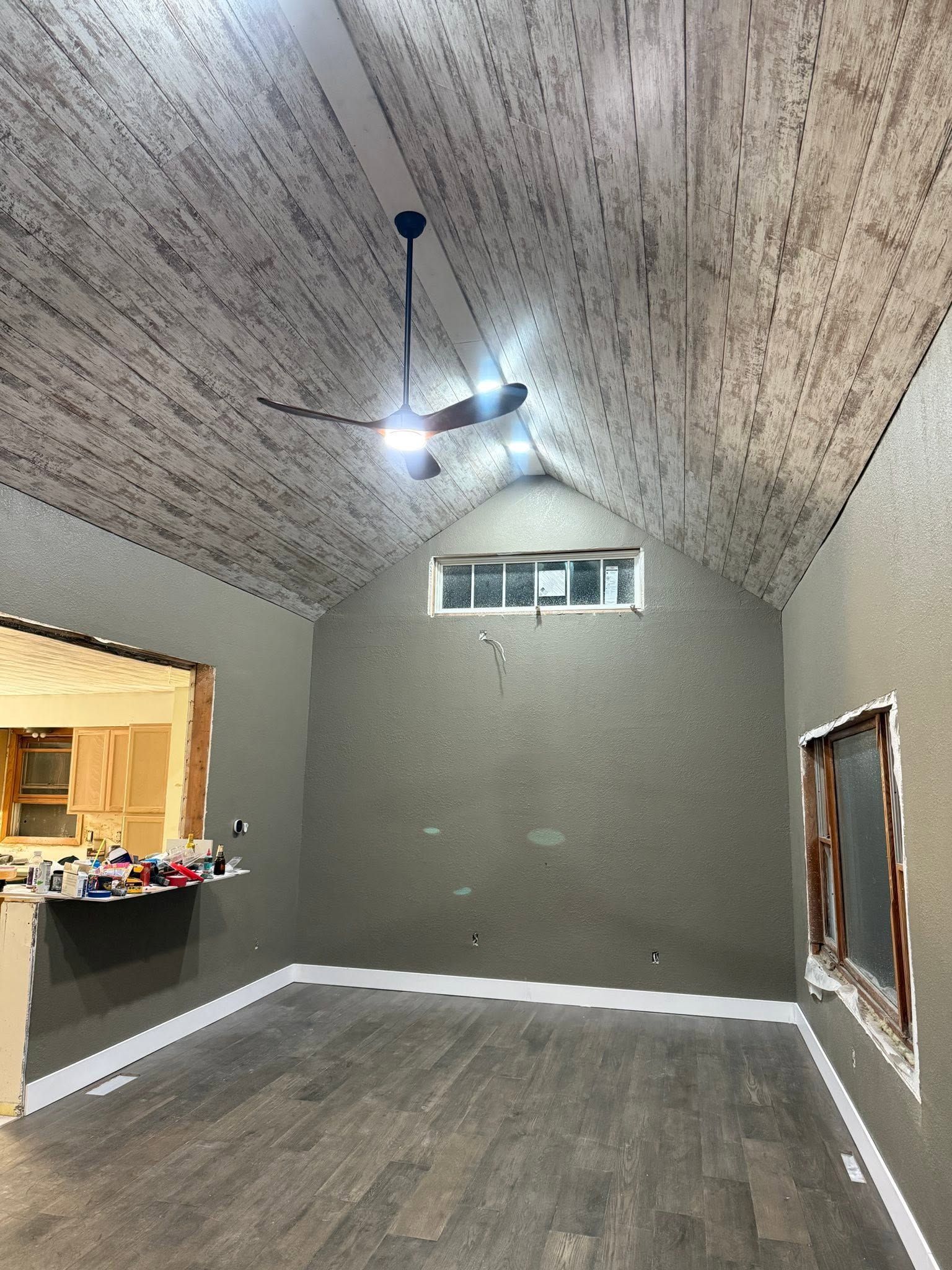 Empty room with sloped ceiling, gray walls, wood floor, ceiling fan, and small windows on one wall