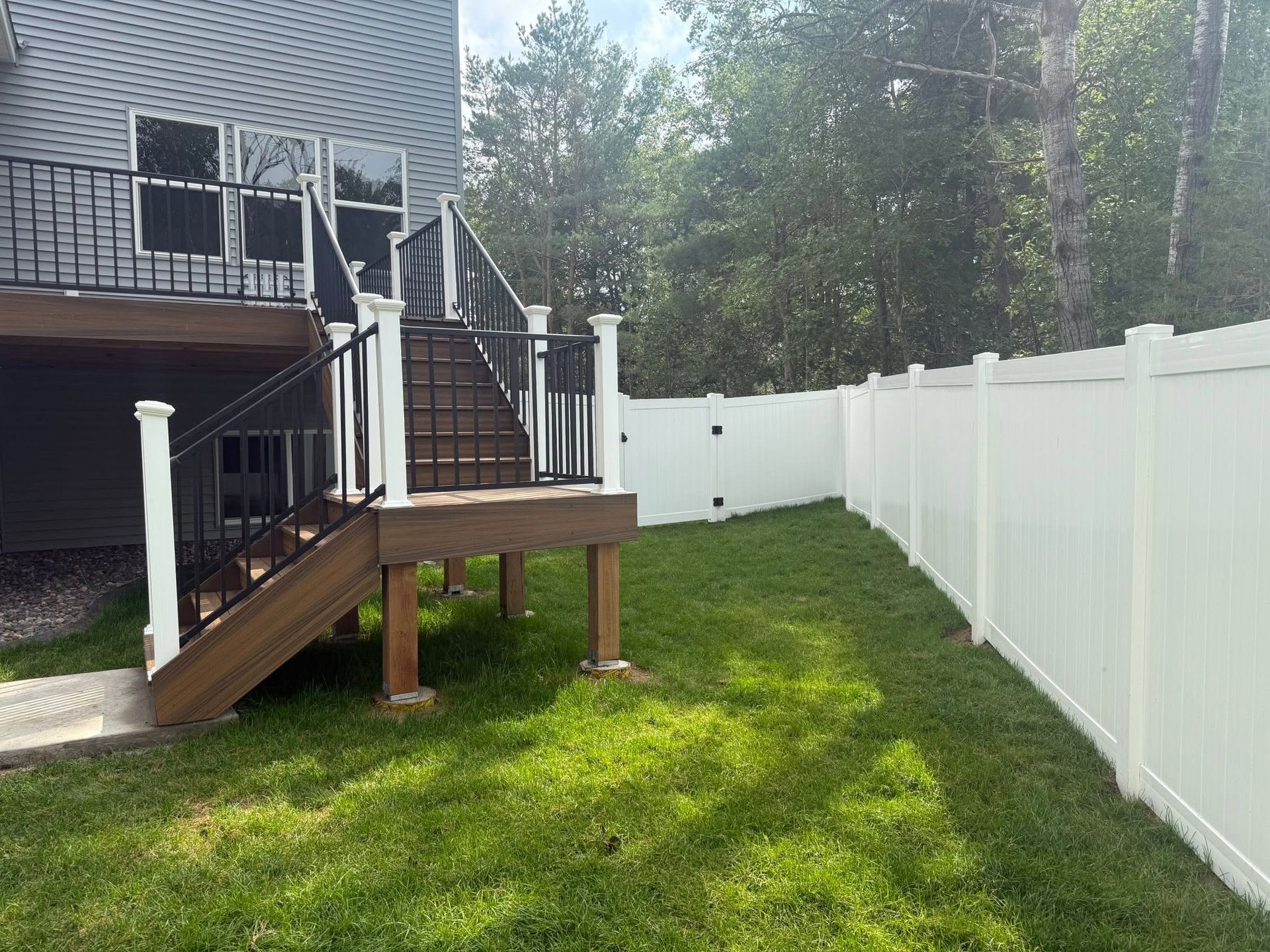 Backyard deck with stairs, white fence, and grassy yard beside a house