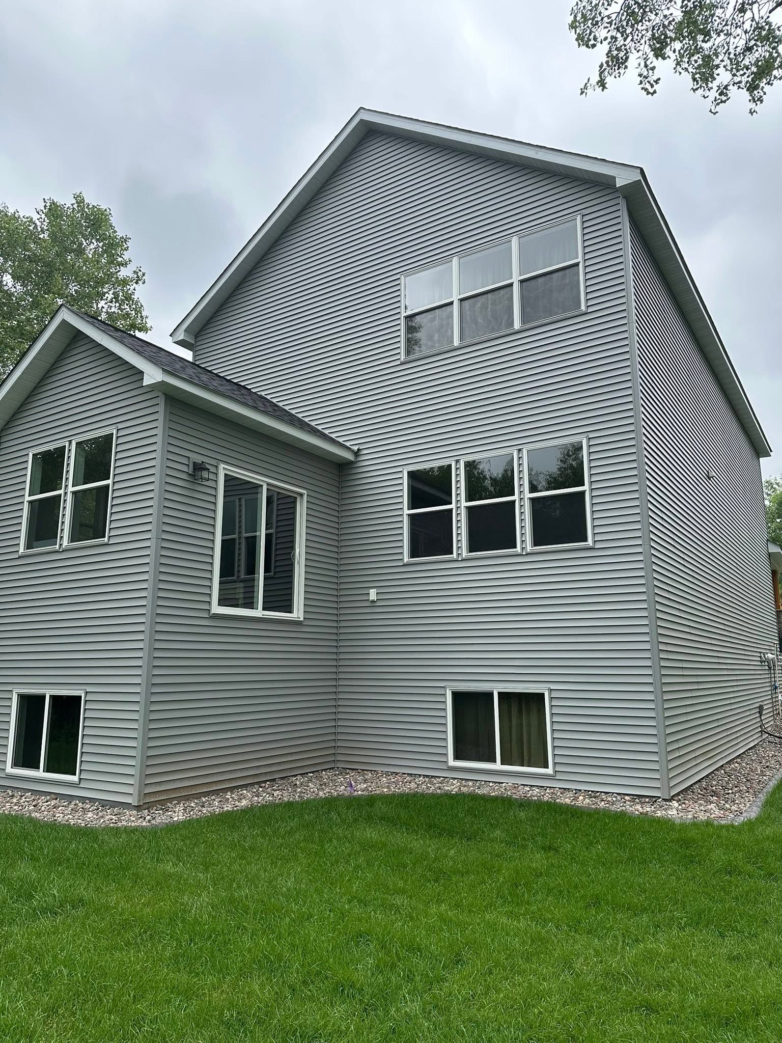 Gray house with wavy-striped siding, white trim, and green lawn under an overcast sky