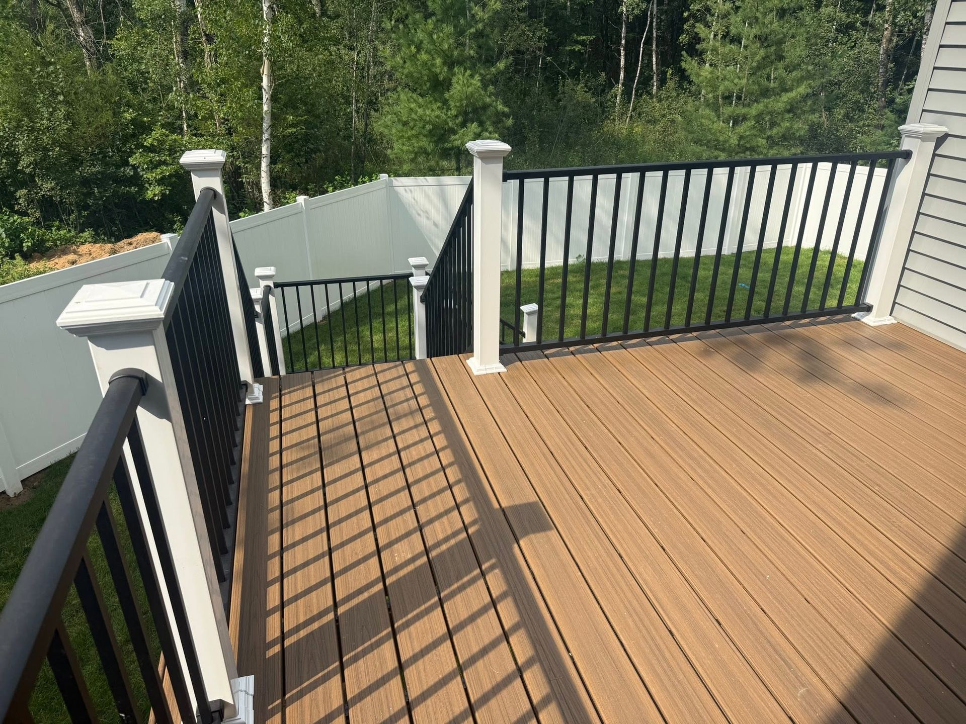 Wooden deck with black railings overlooking a green wooded yard in sunlight