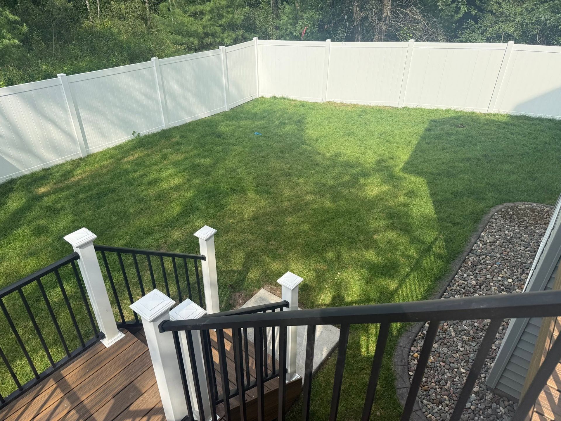 Backyard with green lawn, white privacy fence, and wooden deck with black railing in foreground