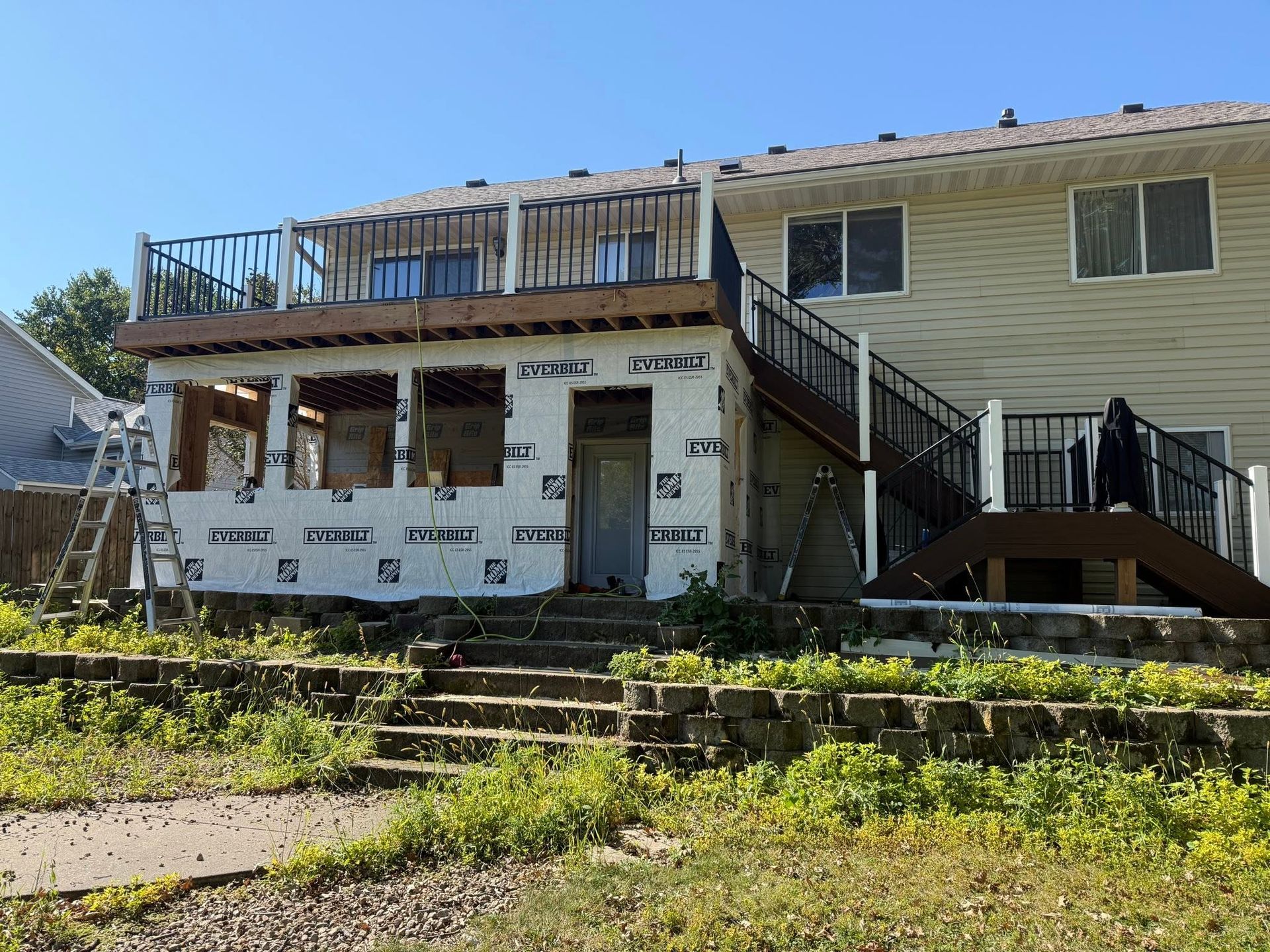 Two-story house with wooden deck and exterior stairs, sunlit with a partially damaged front facade