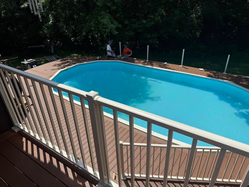 Backyard swimming pool with blue water and wooden deck, viewed from behind a railing