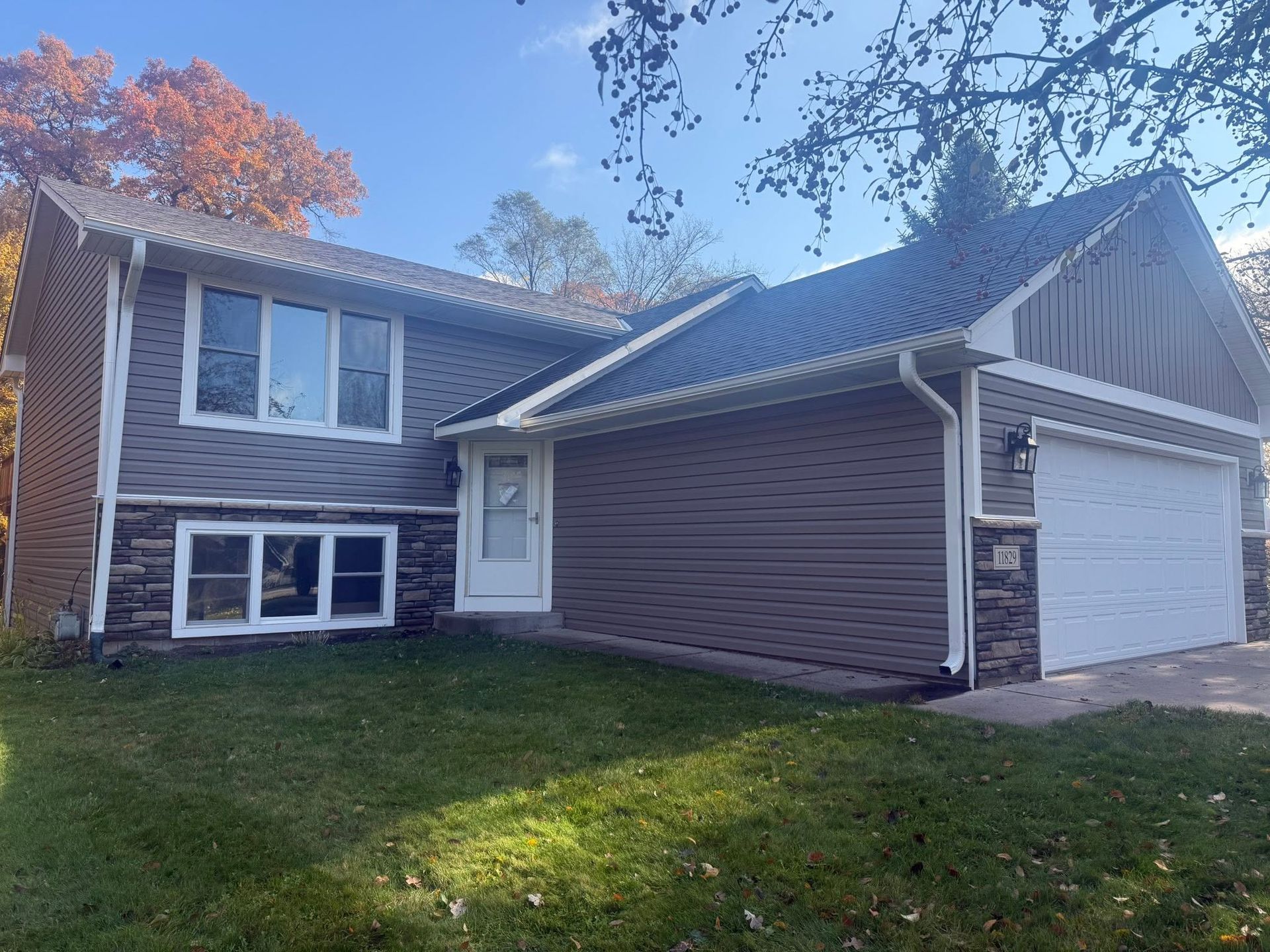 Two-story suburban house with brick and siding, attached garage, and front lawn under a blue sky