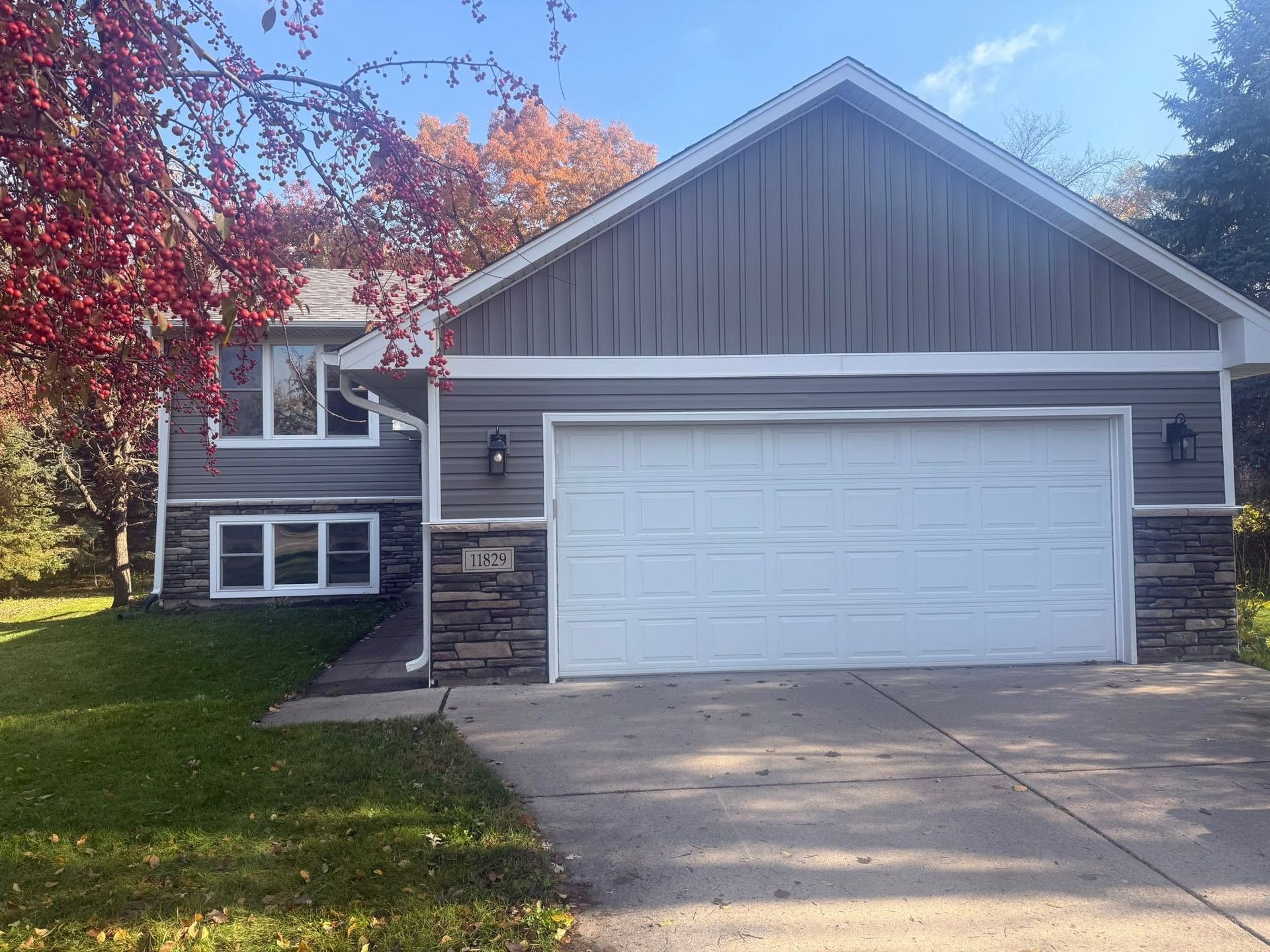 Suburban house with white garage door, stone accents, and a red tree in the front yard