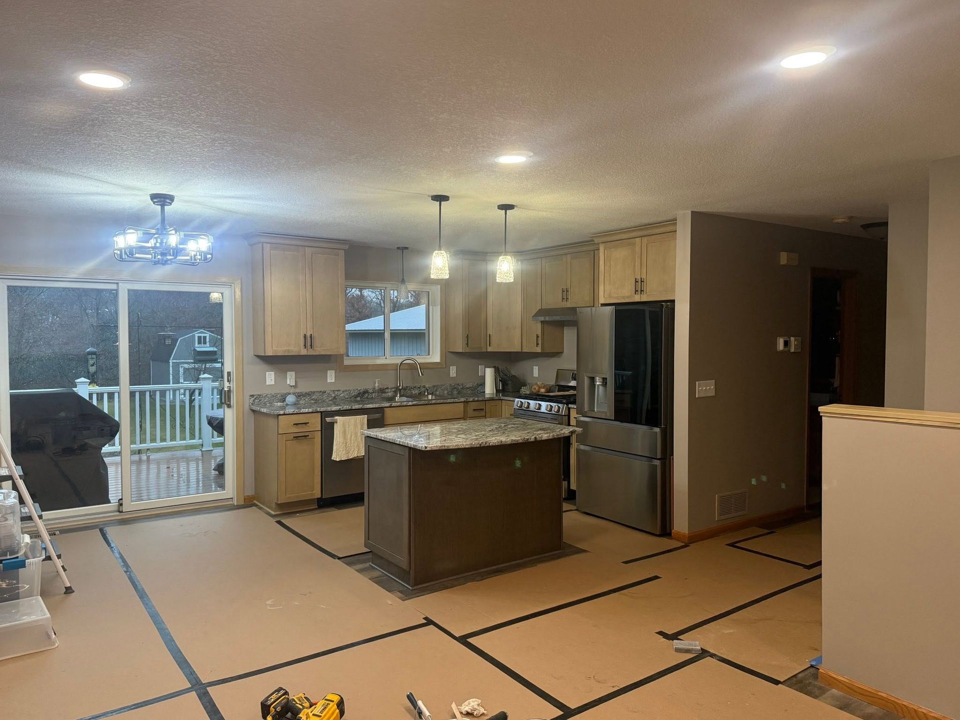 Kitchen with island, stainless fridge, wood cabinets, and taped-off floor in a home under renovation