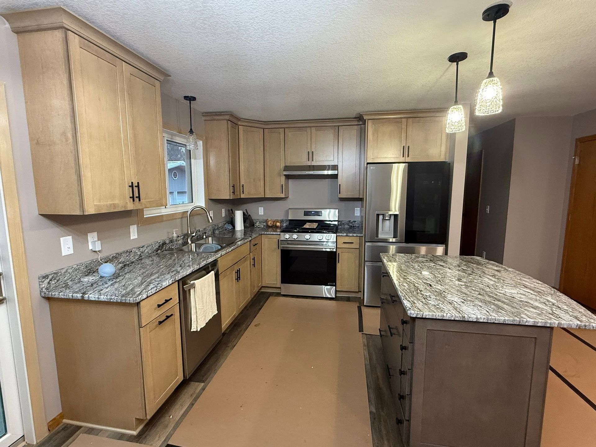 Bright modern kitchen with light wood cabinets, granite counters, stainless steel appliances, and pendant lights.
