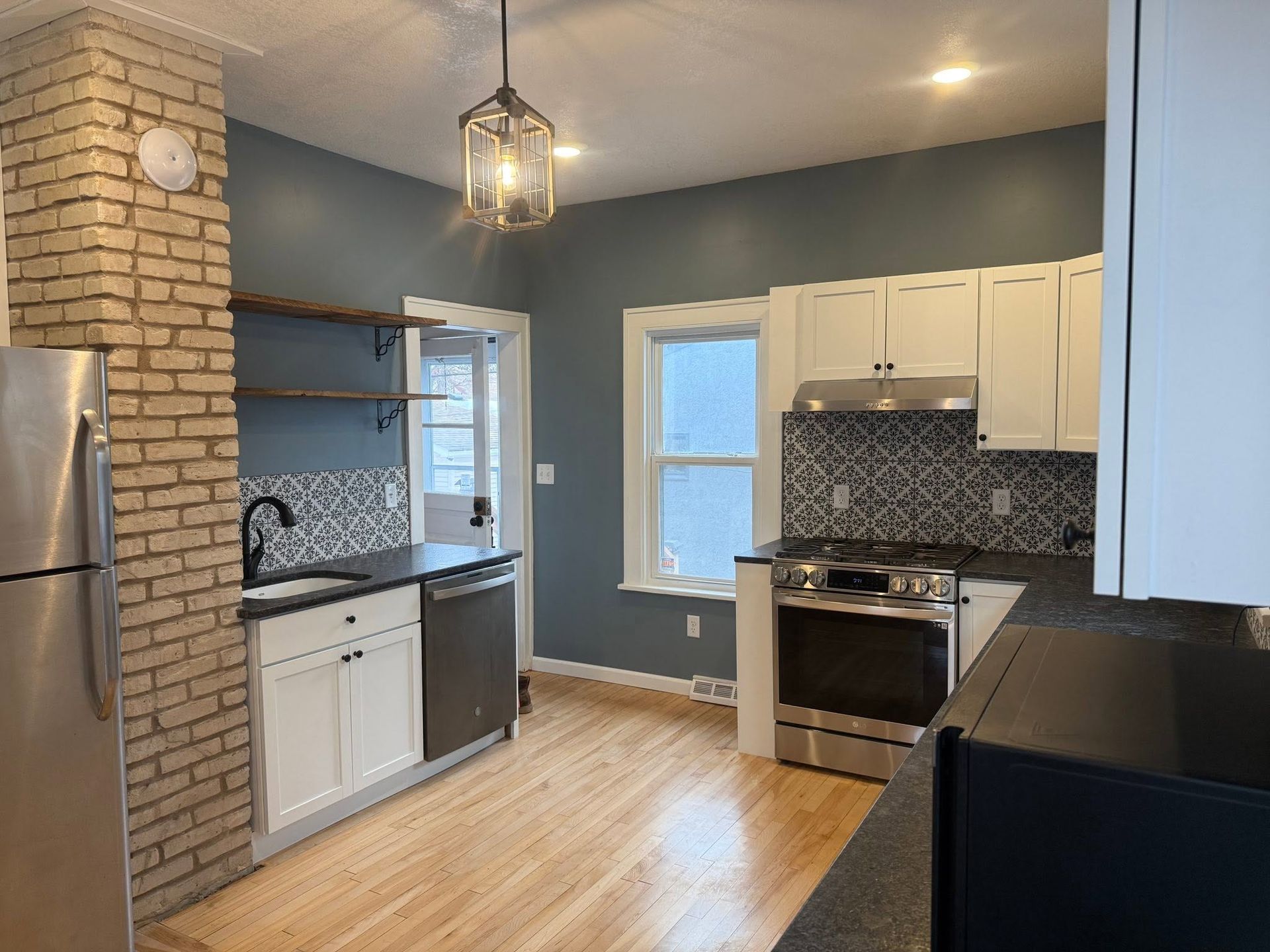 Empty kitchen with brick column, blue-gray walls, white cabinets, and hardwood floors