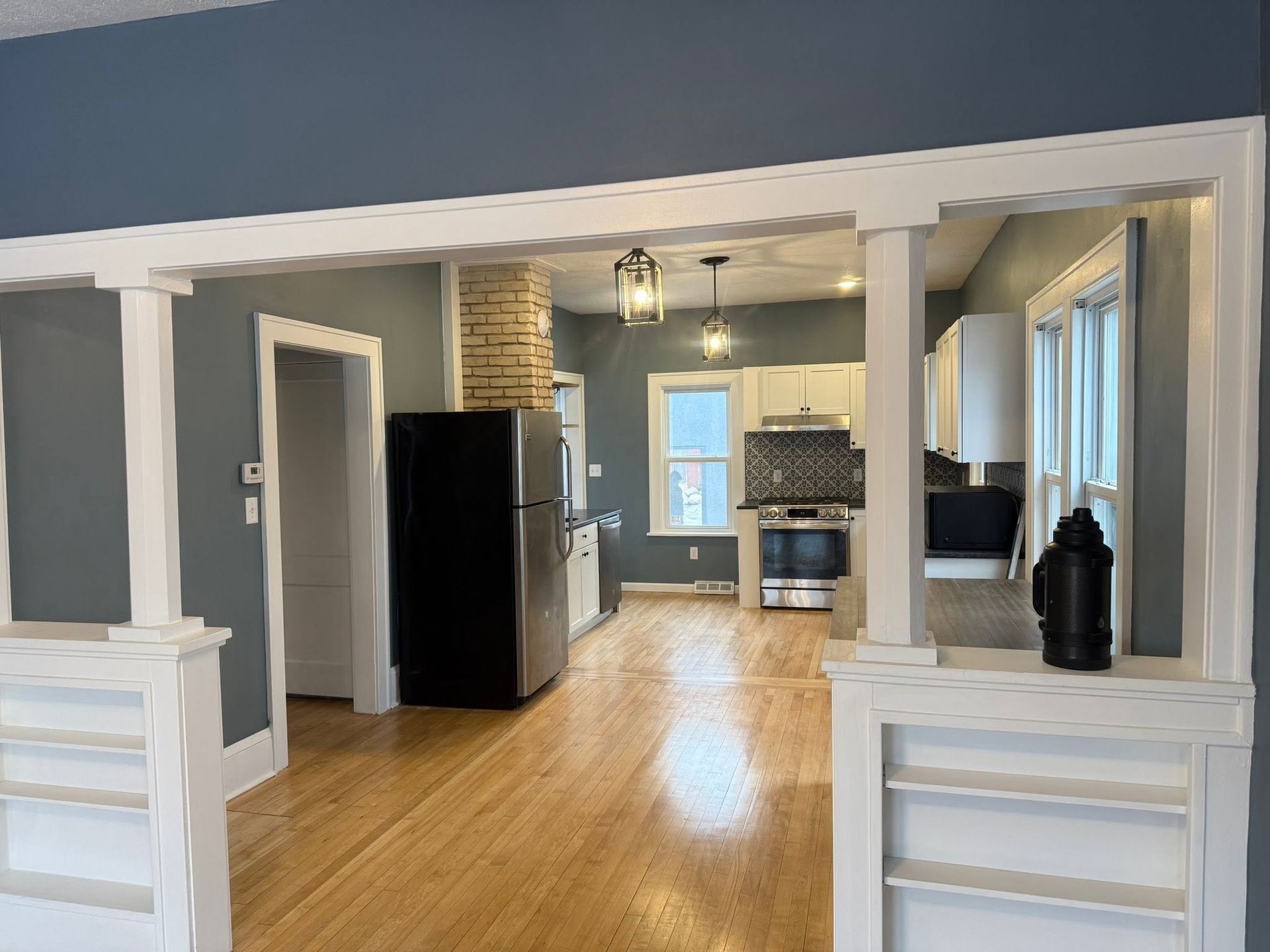 Open kitchen and living room with blue walls, white trim, hardwood floors, and a black refrigerator.
