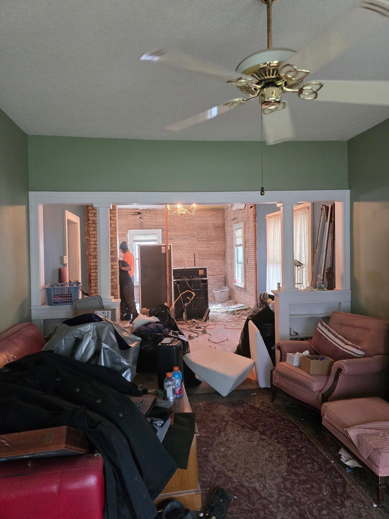 Cluttered living room with red sofas, ceiling fan, and wide open doorway to a brick patio
