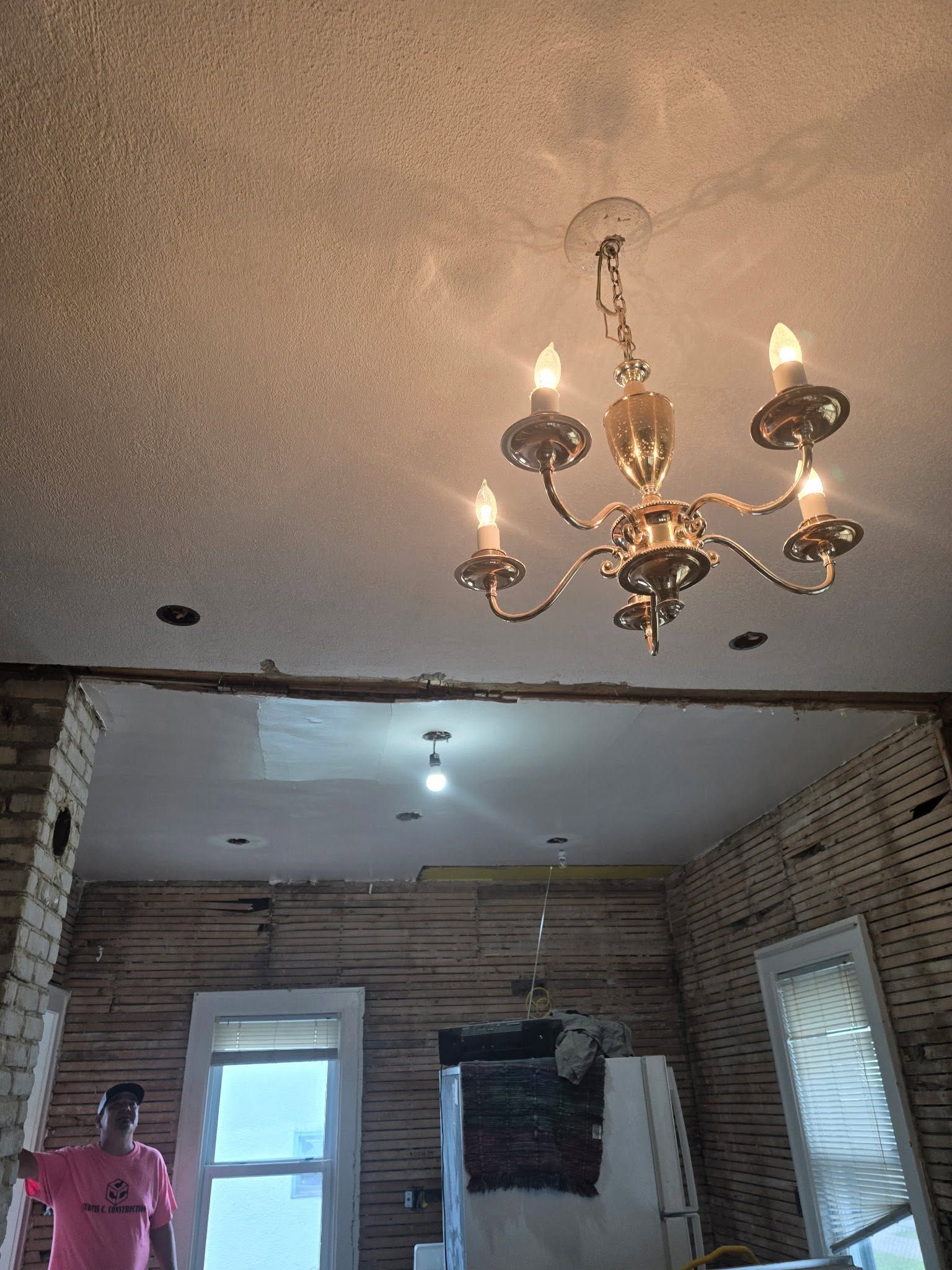 Partially renovated room with exposed brick walls, two ceiling lights, and a chandelier; person standing at left.