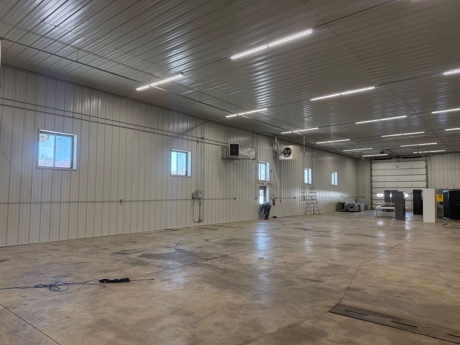Large empty industrial warehouse with concrete floor, white walls, and a high ceiling with lights.