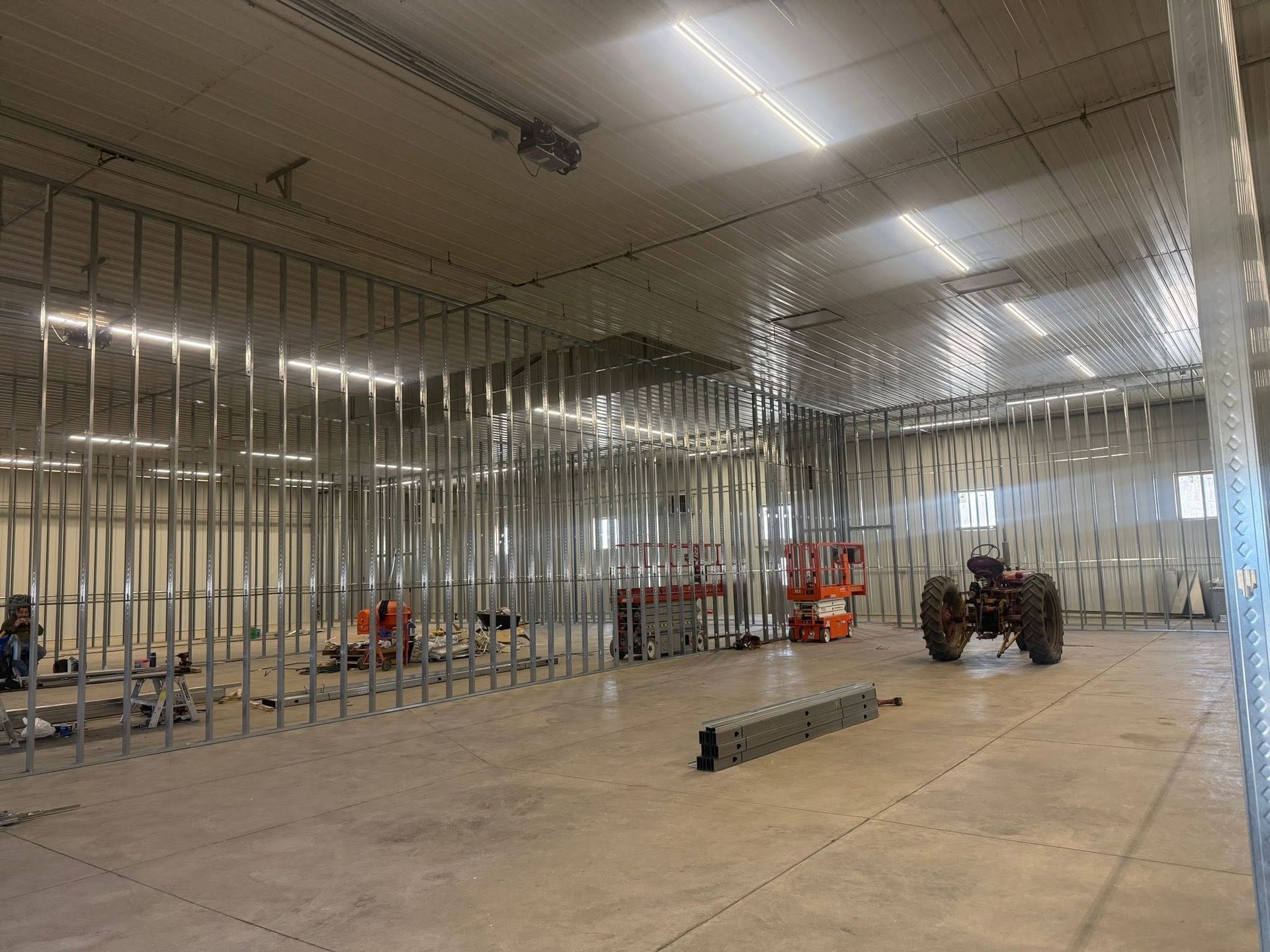 Interior of a building under construction with metal wall framing, exposed ceiling, and equipment on a concrete floor