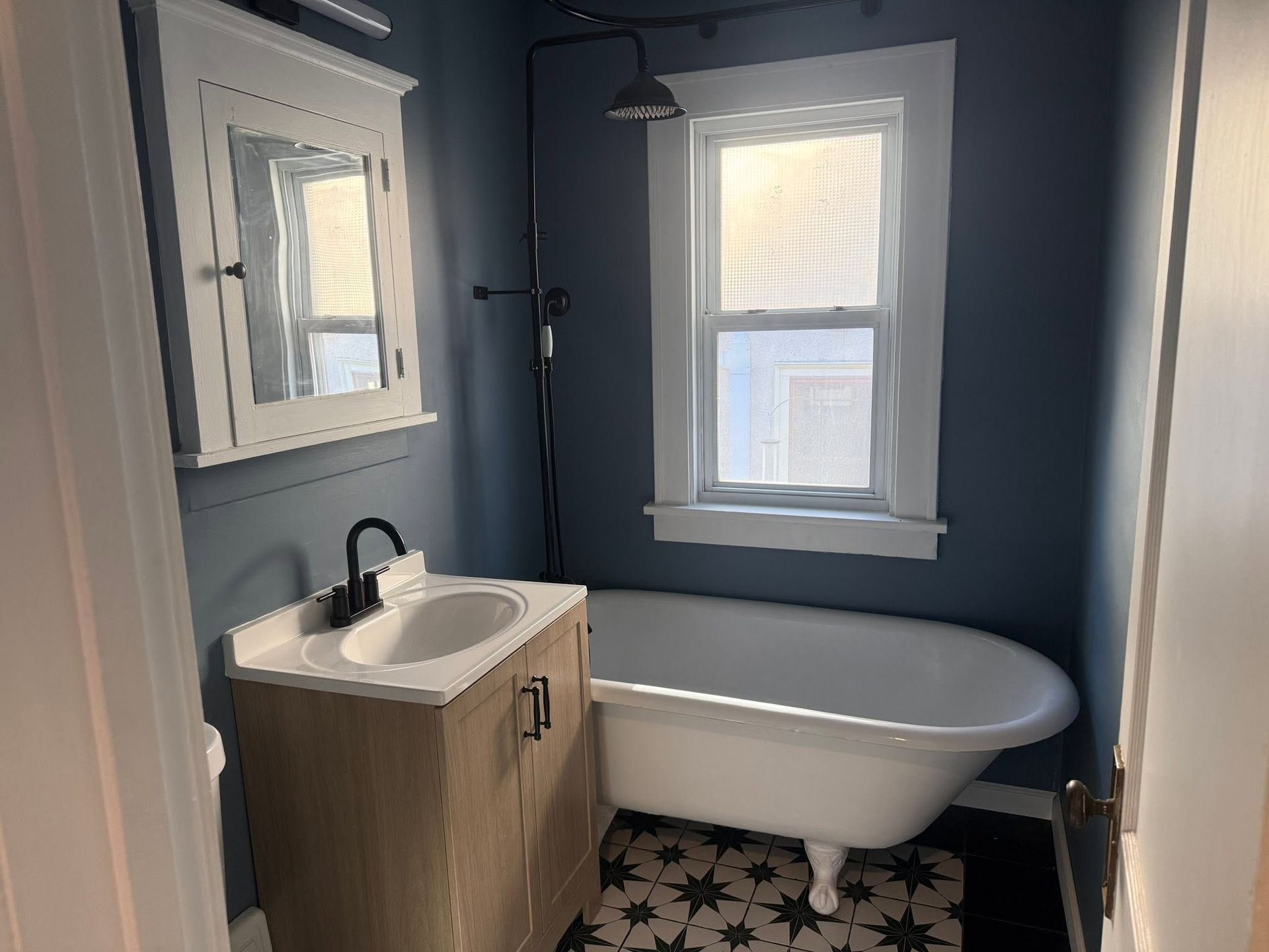 Small blue bathroom with a sink, mirror, window, and freestanding bathtub