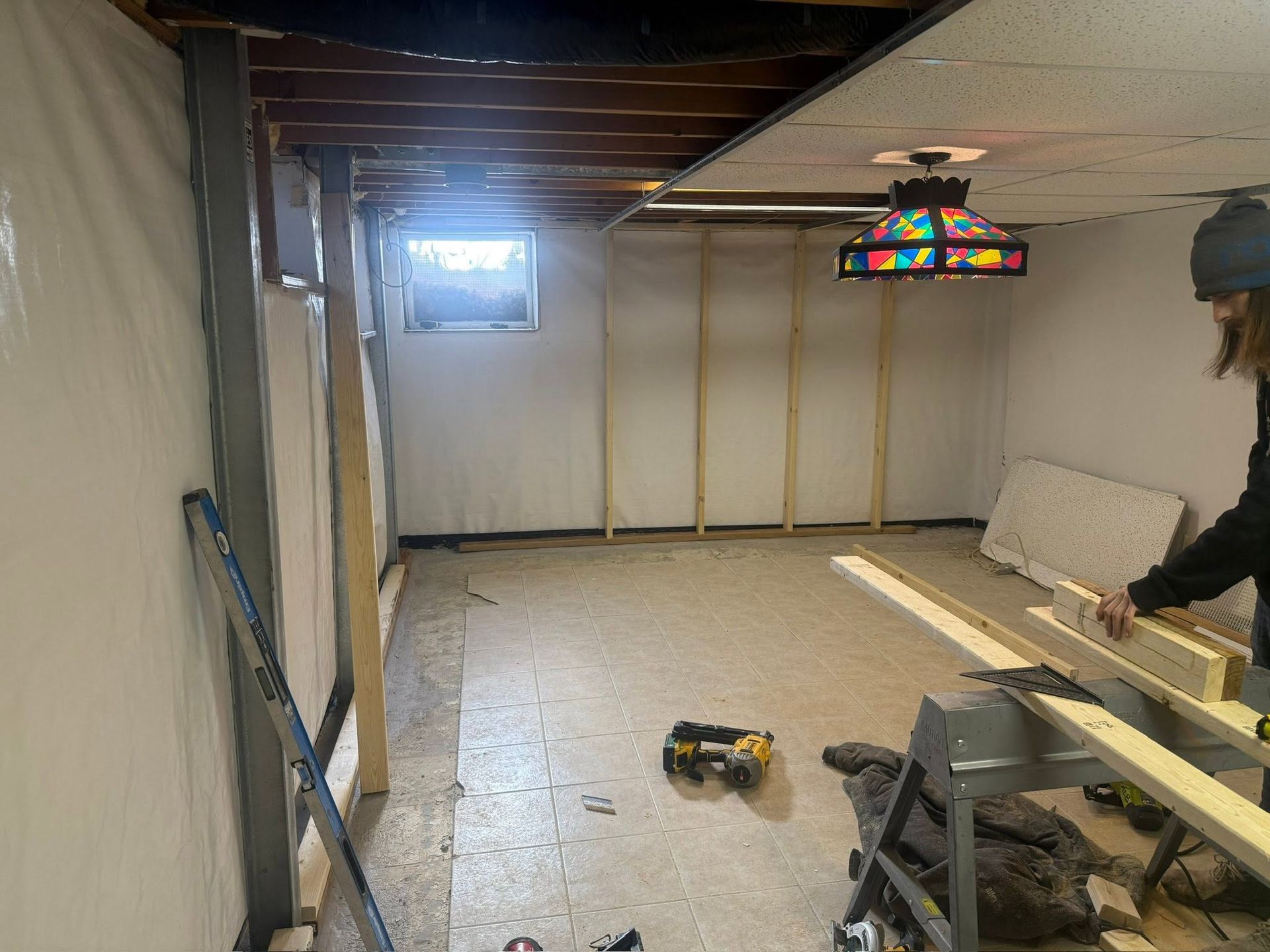 Basement under renovation with exposed ceiling, tools on floor, and a workbench against the wall