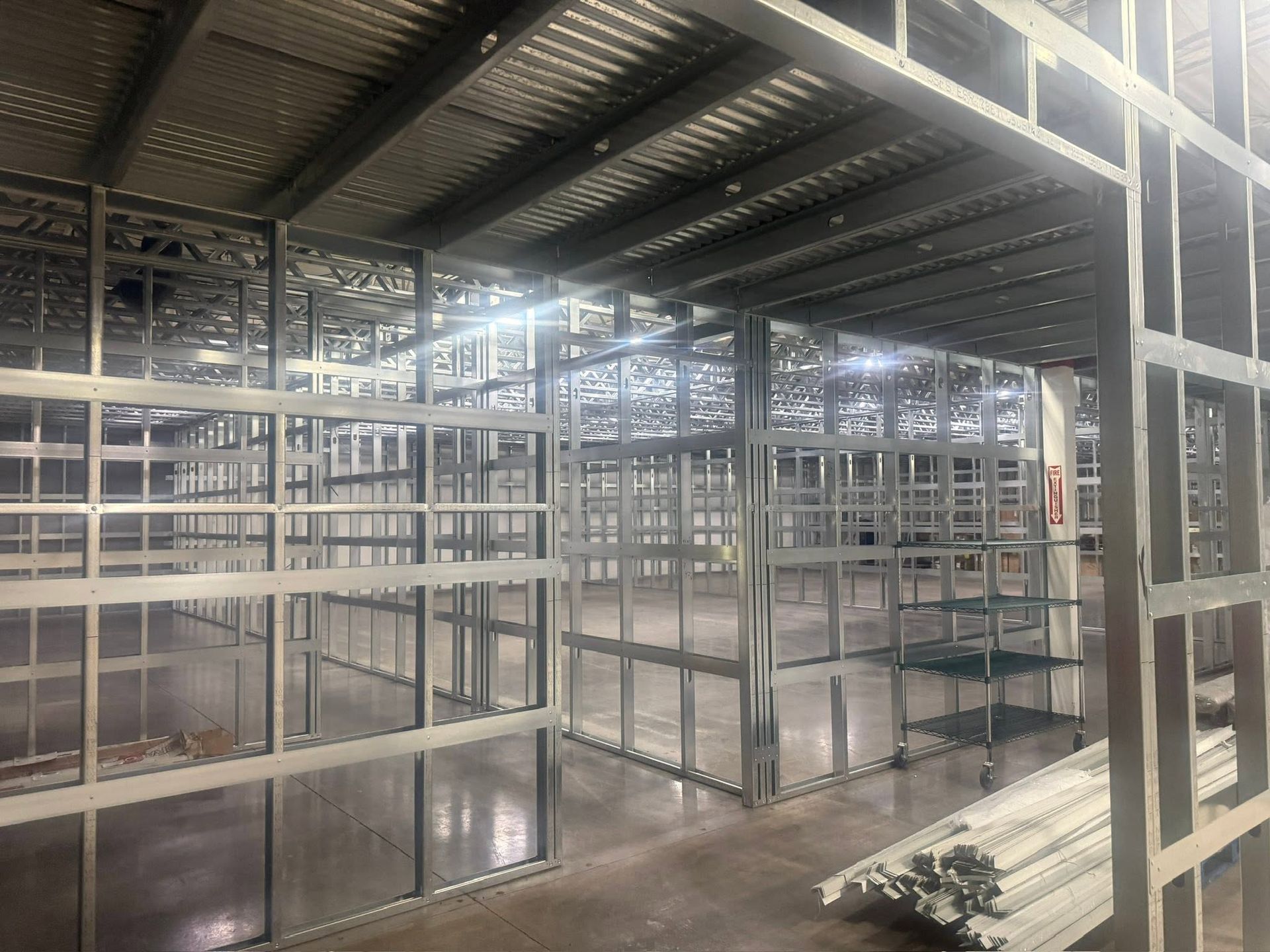 Metal-framed interior under construction with glass walls and stacked white pipes on the floor