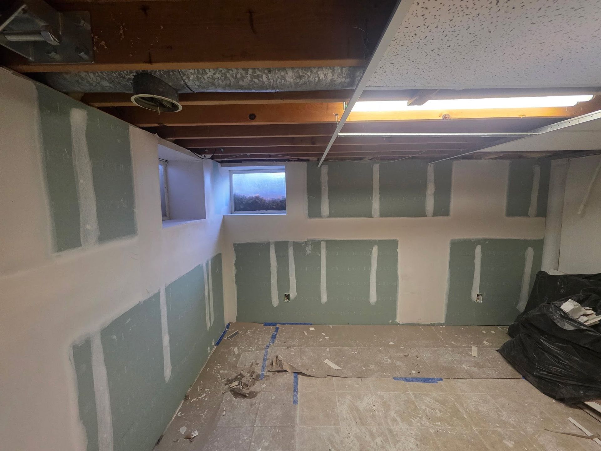 Unfinished basement room with drywall patches, exposed ceiling joists, and a small window.