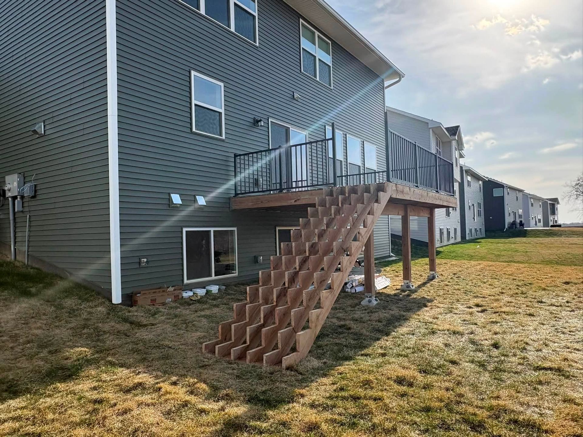 Back deck with wooden stairs on a brick apartment building, beside a grassy yard