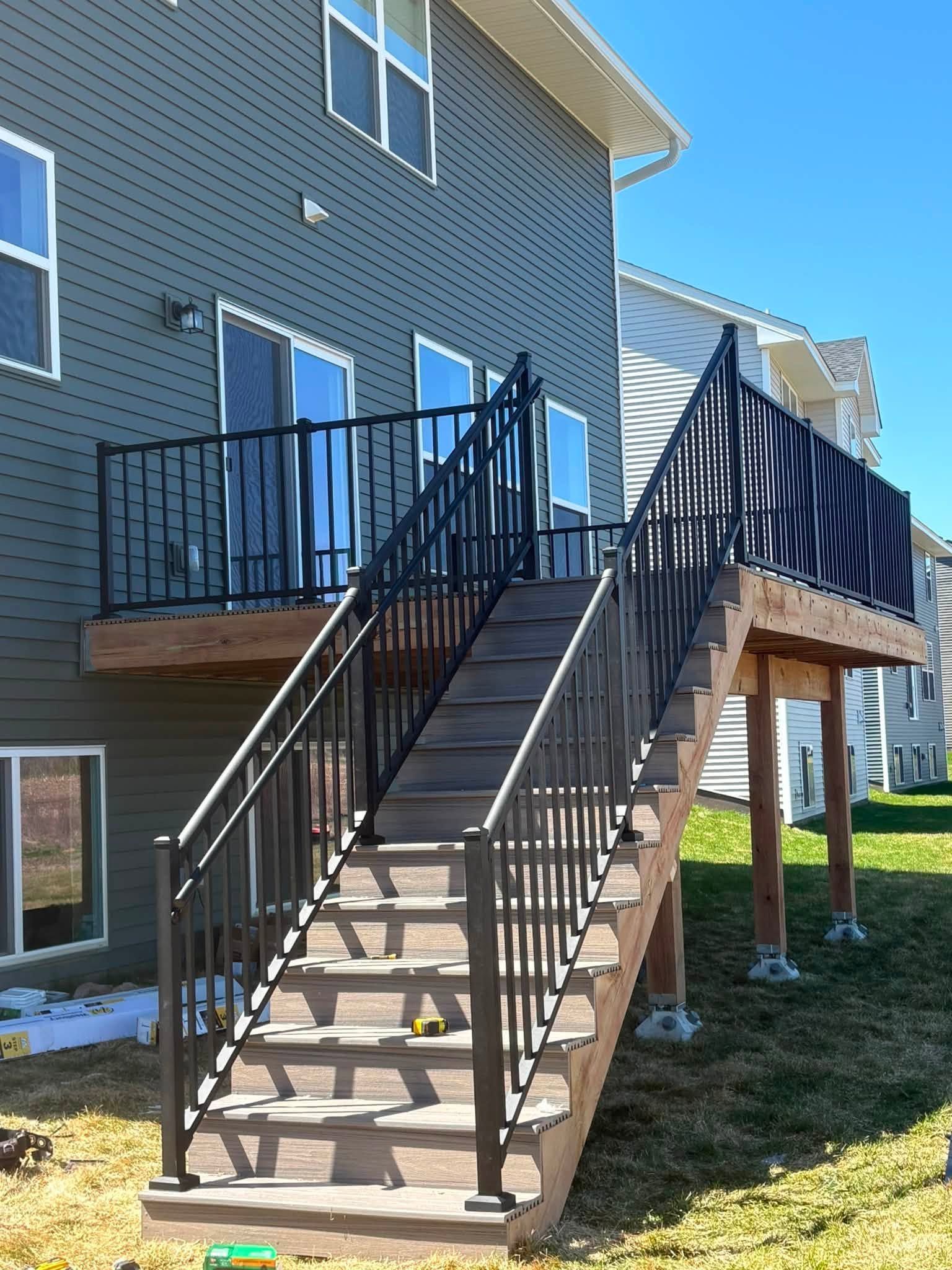 Exterior wooden staircase with black railings leading to an elevated deck beside a blue house.