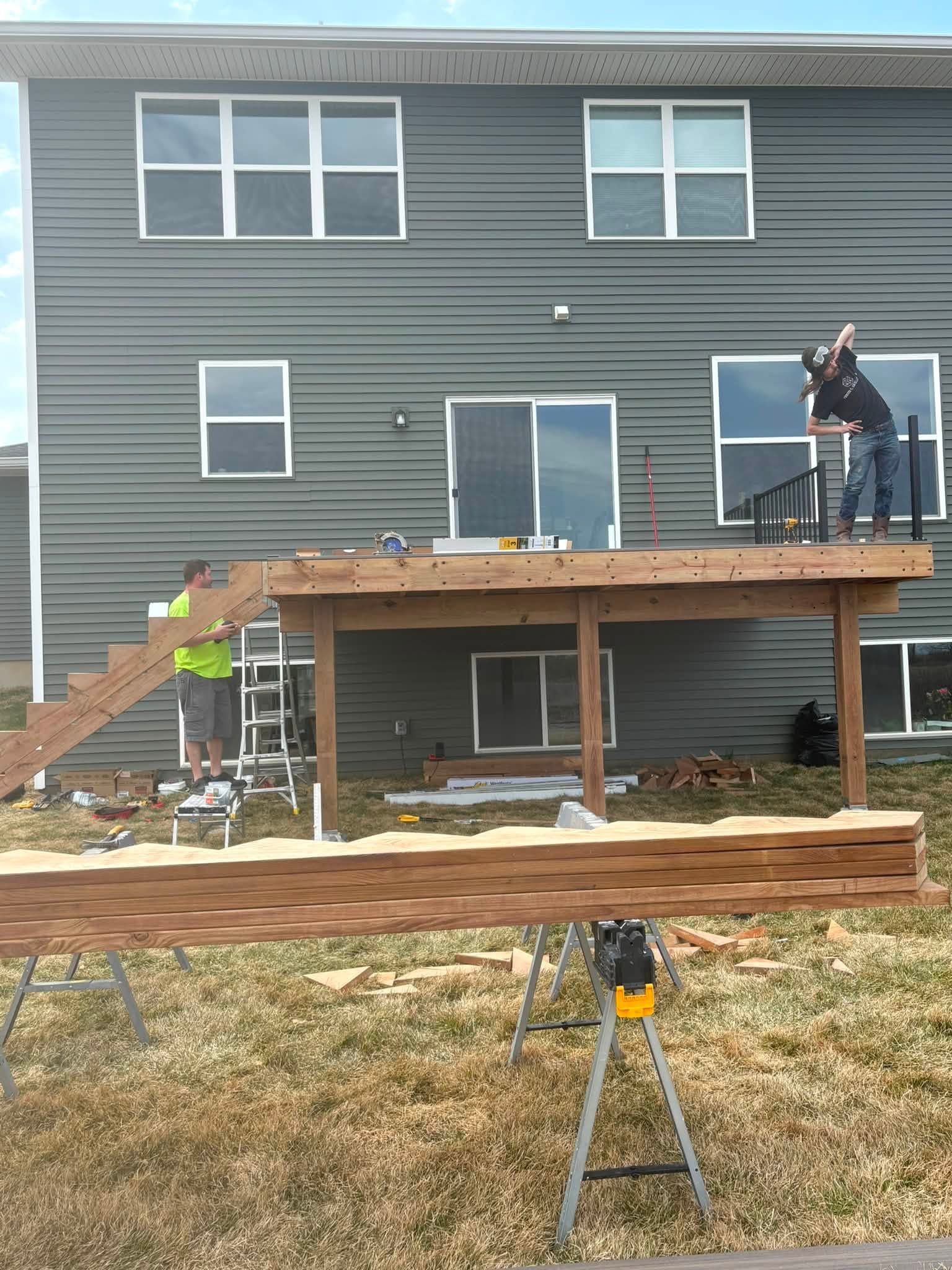 House under construction with workers on an elevated deck and a tripod in the foreground