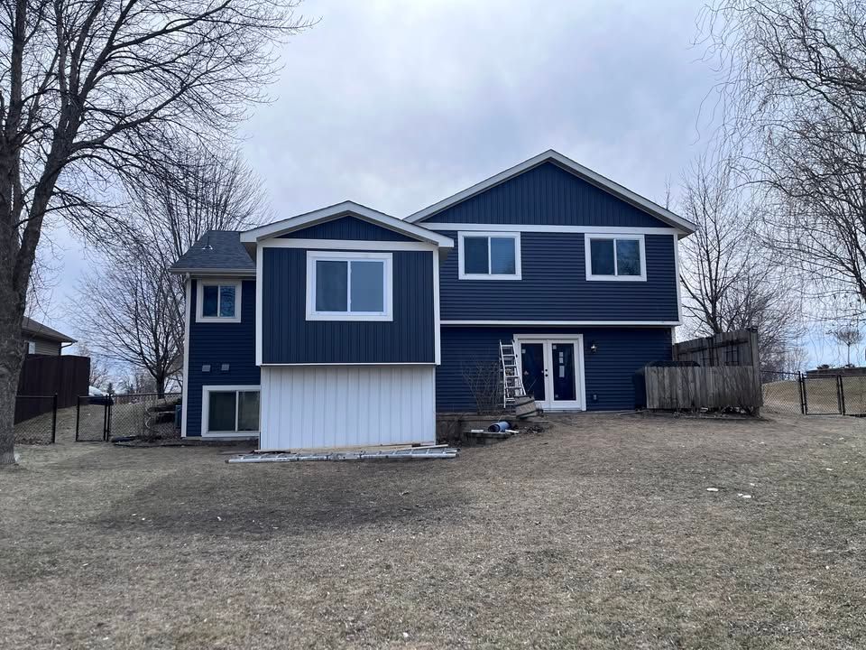 Blue two-story house with white trim and a small covered entrance in a leafless yard