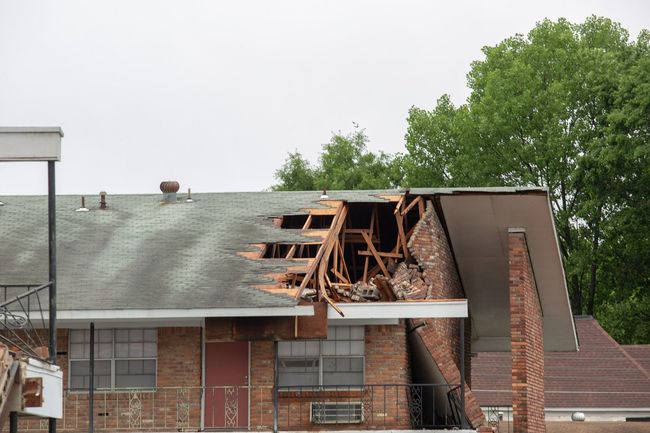 Damaged roof and brick building with exposed beams and storm debris under cloudy sky
