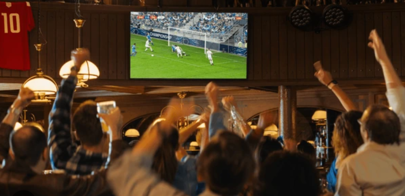 A group of people are watching a soccer game on a television in a bar.