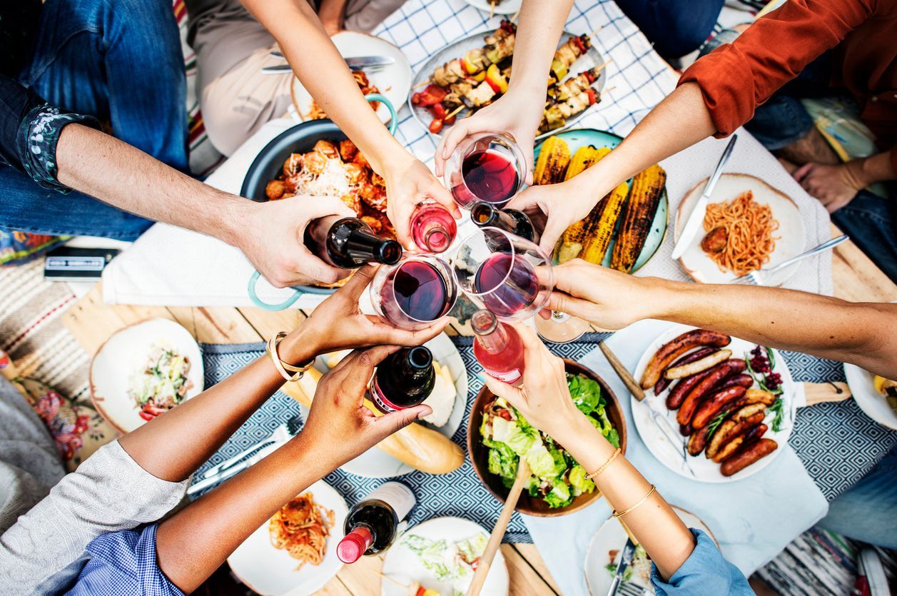 A group of people are toasting with wine glasses at a picnic table.
