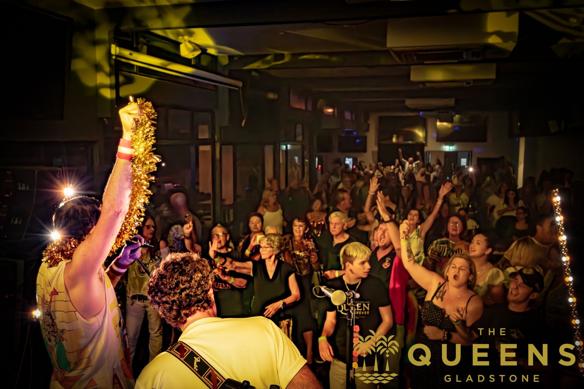 A man is playing a guitar in front of a crowd at a concert called the queens