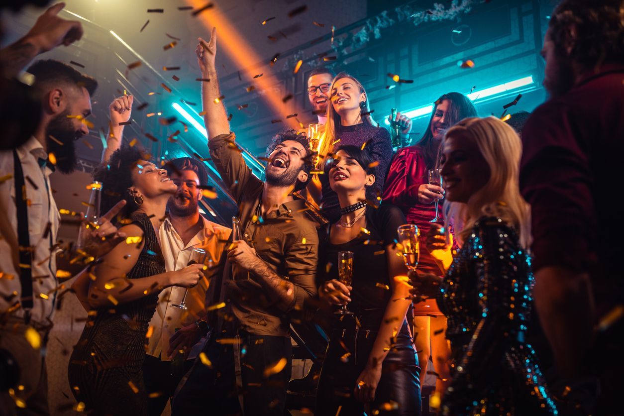 A group of people are dancing in a club with confetti falling from the ceiling.
