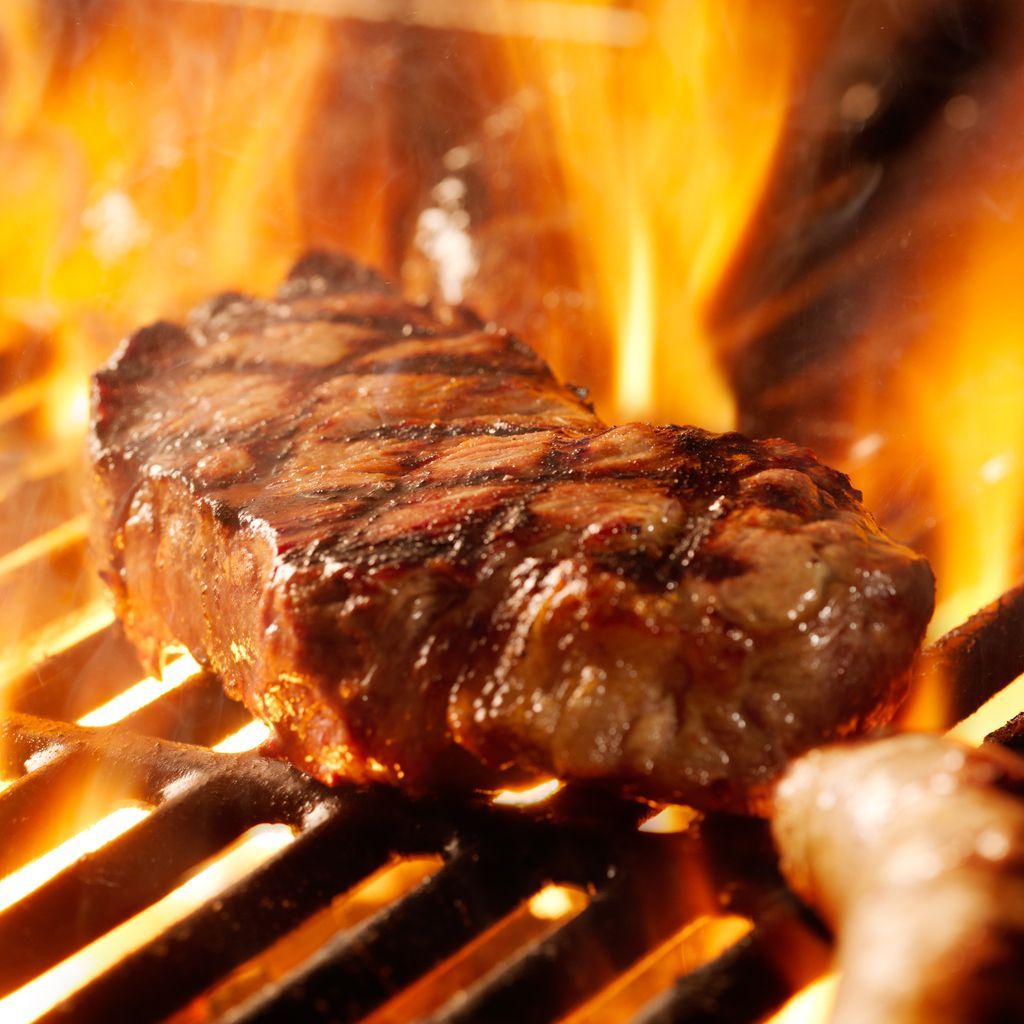 A steak is cooking on a grill with flames behind it