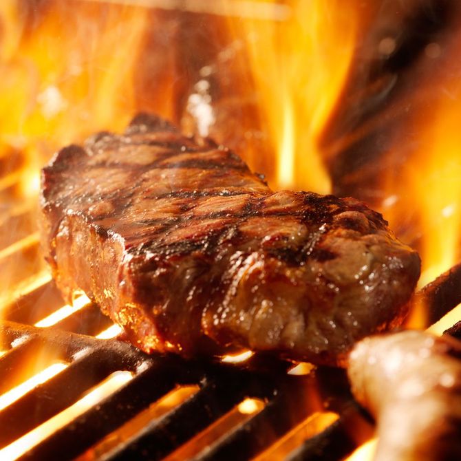 A steak is cooking on a grill with flames behind it