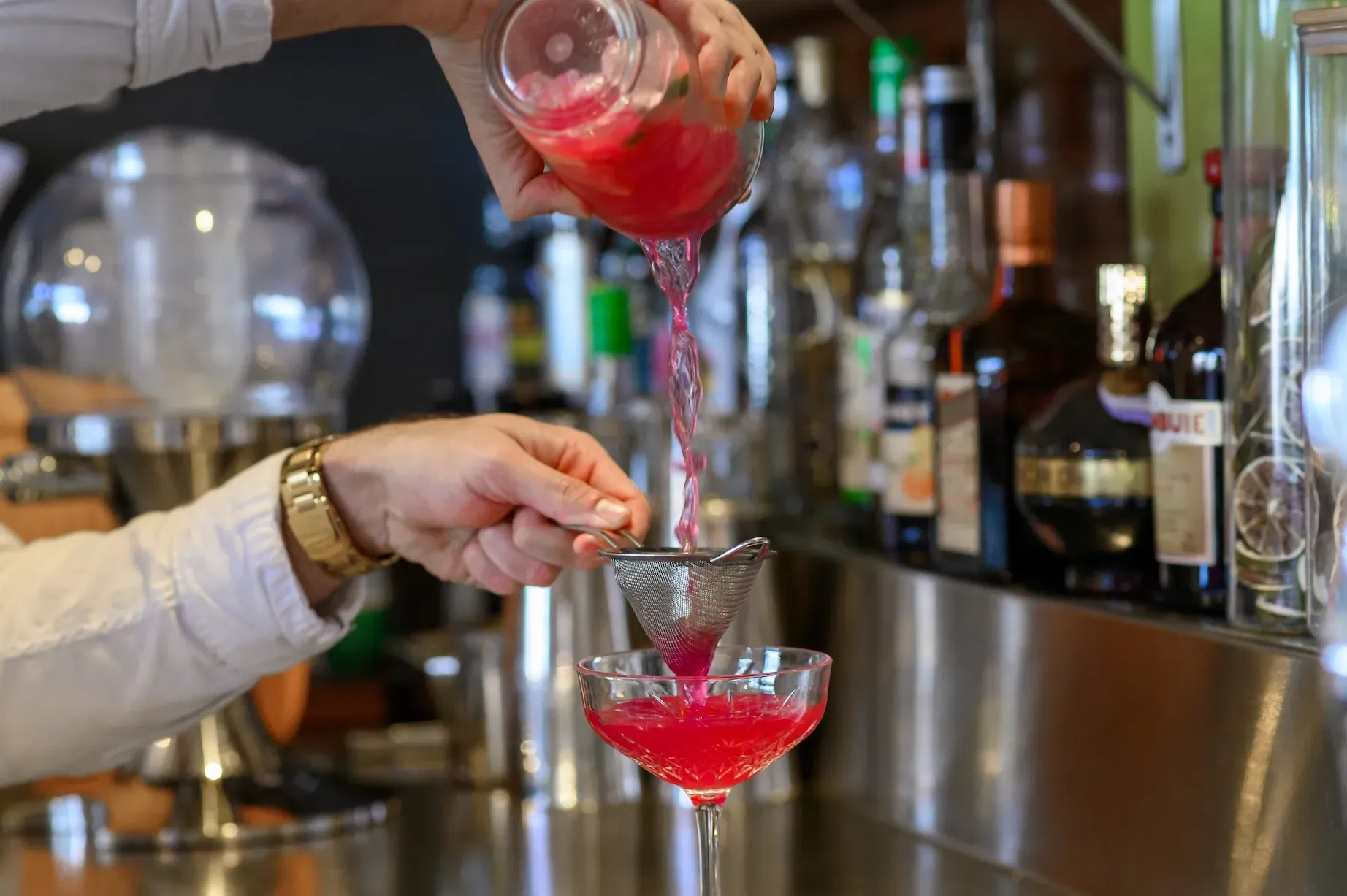 A bartender is pouring a red drink into a glass.