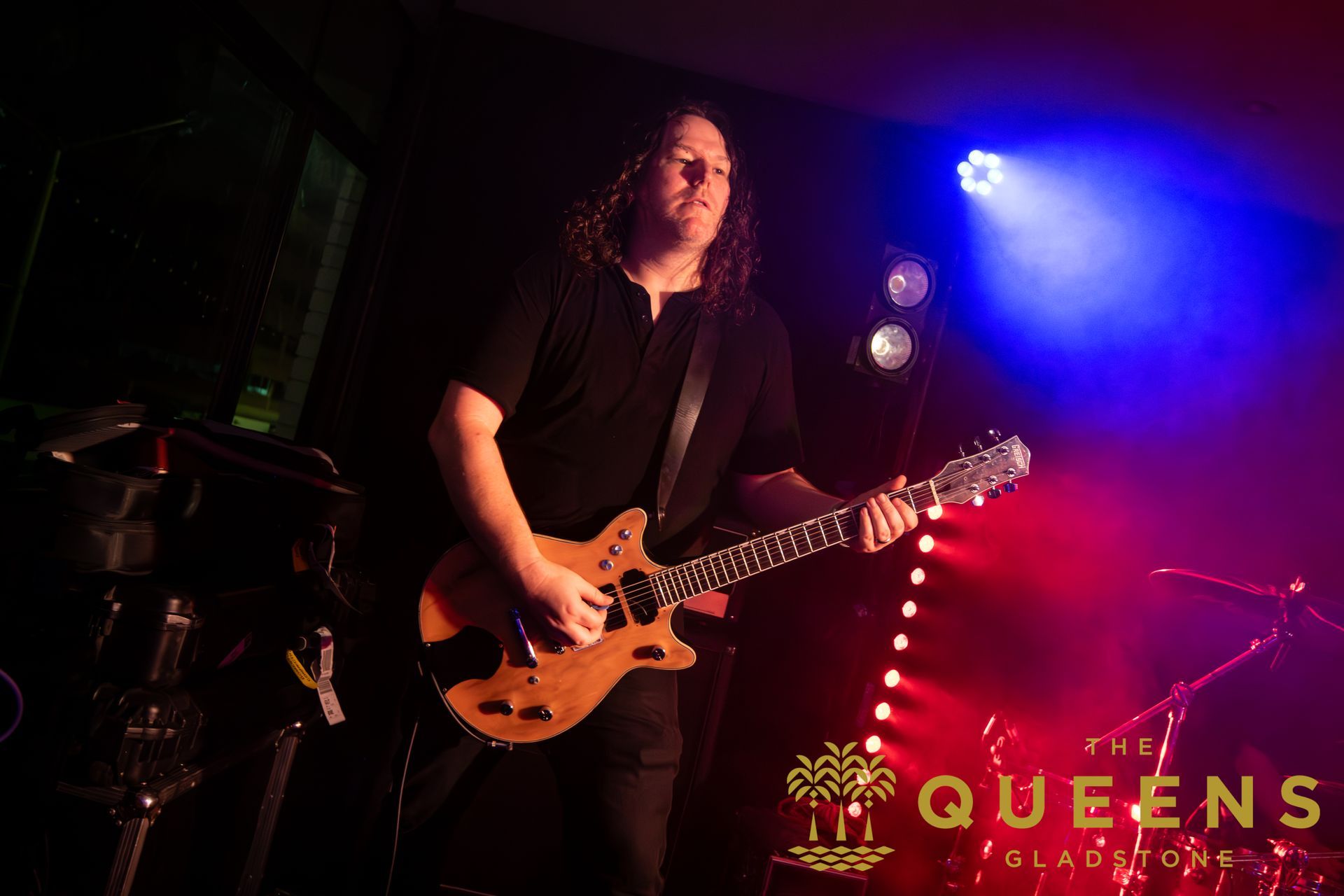Guitarist performing onstage under red and blue lights at Queens nightclub