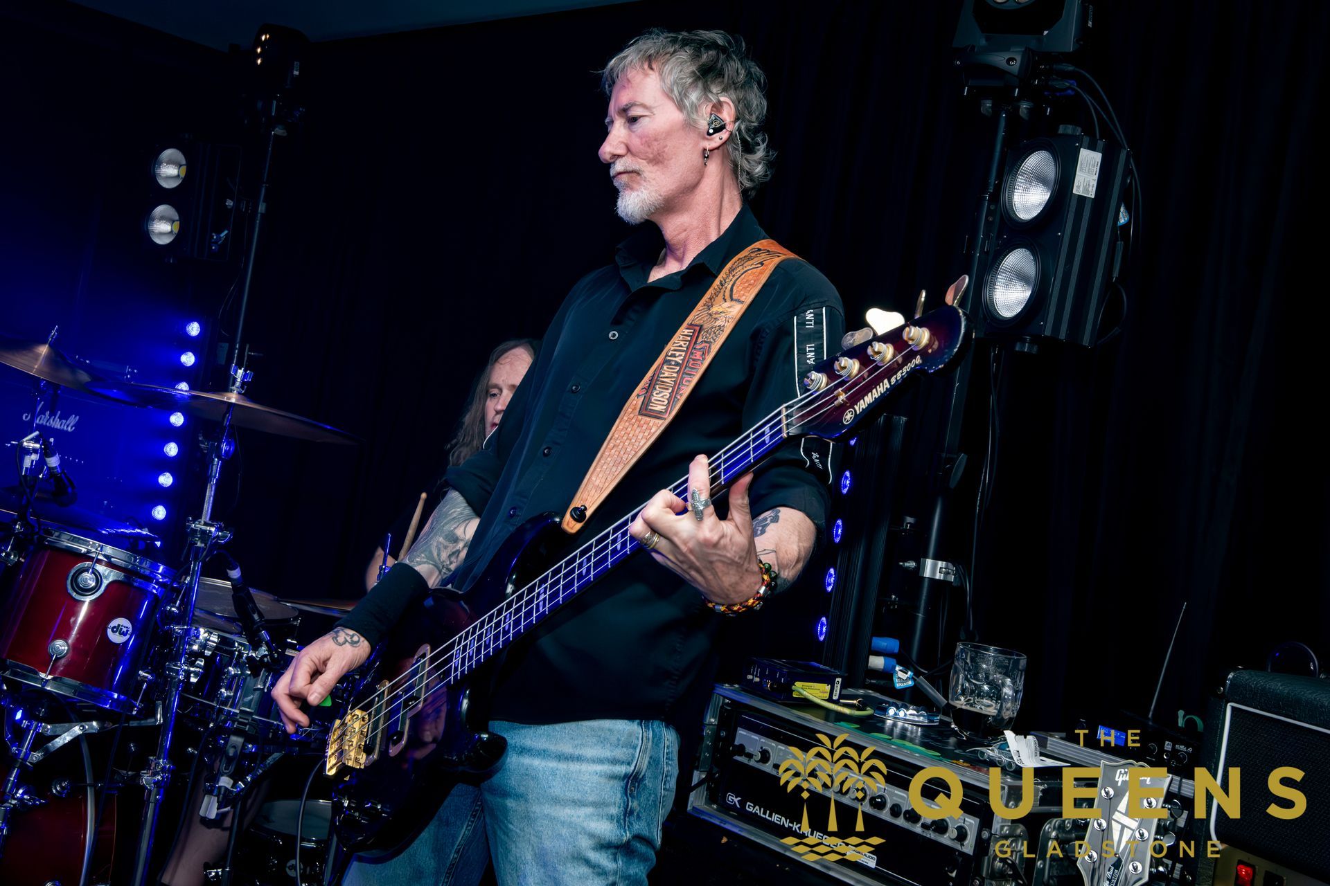 Guitarist performing on a dark stage with blue lighting and drums in the background
