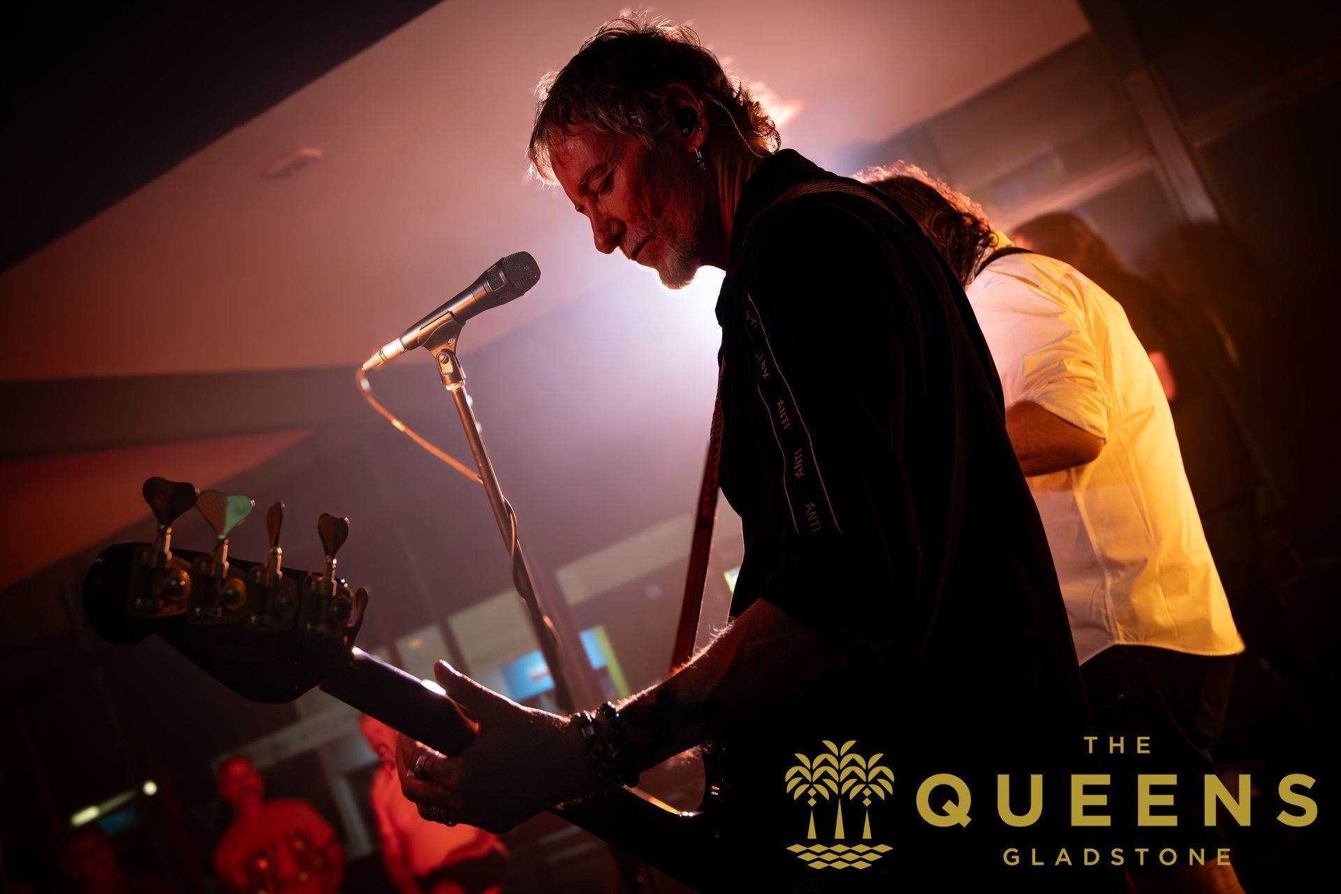 Live band performing on stage under pink and orange lights at The Queens, Glasgow