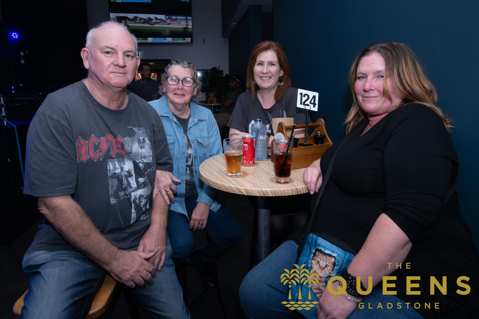 Four people seated at a small table in a dimly lit lounge, smiling with drinks and a table number sign.