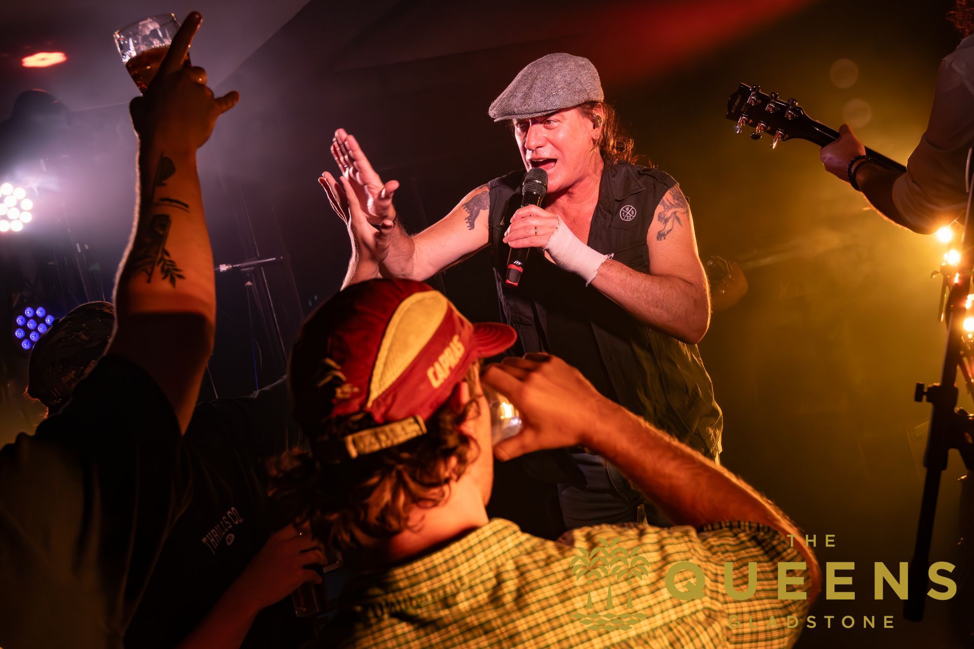Singer in gray cap performing on a dimly lit stage, reaching toward the crowd with warm orange lights.