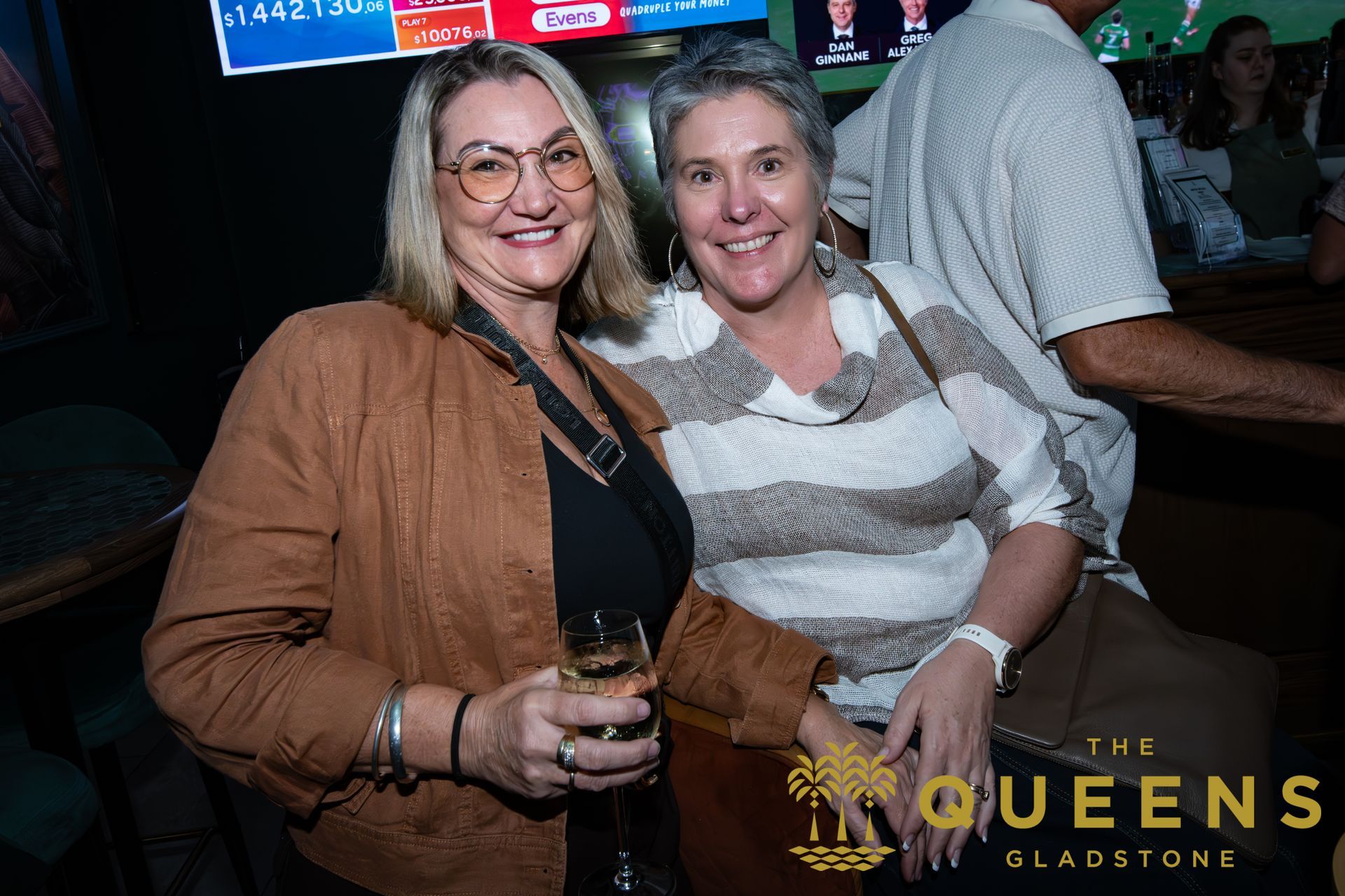 Two smiling people posing at a dimly lit venue, one holding a drink.