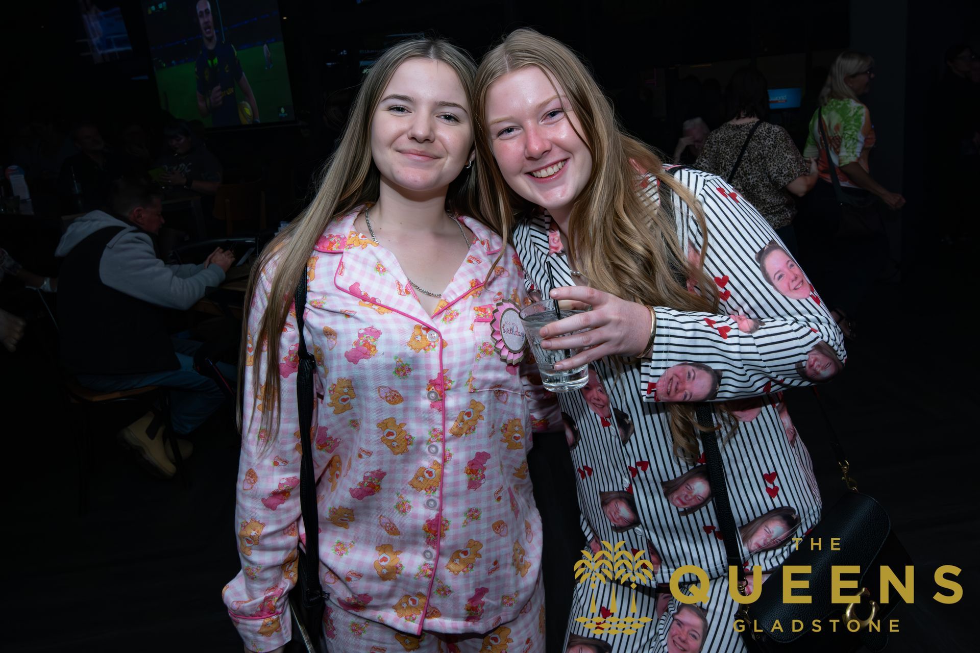 Two smiling friends pose together at a dimly lit event, wearing colorful patterned tops.