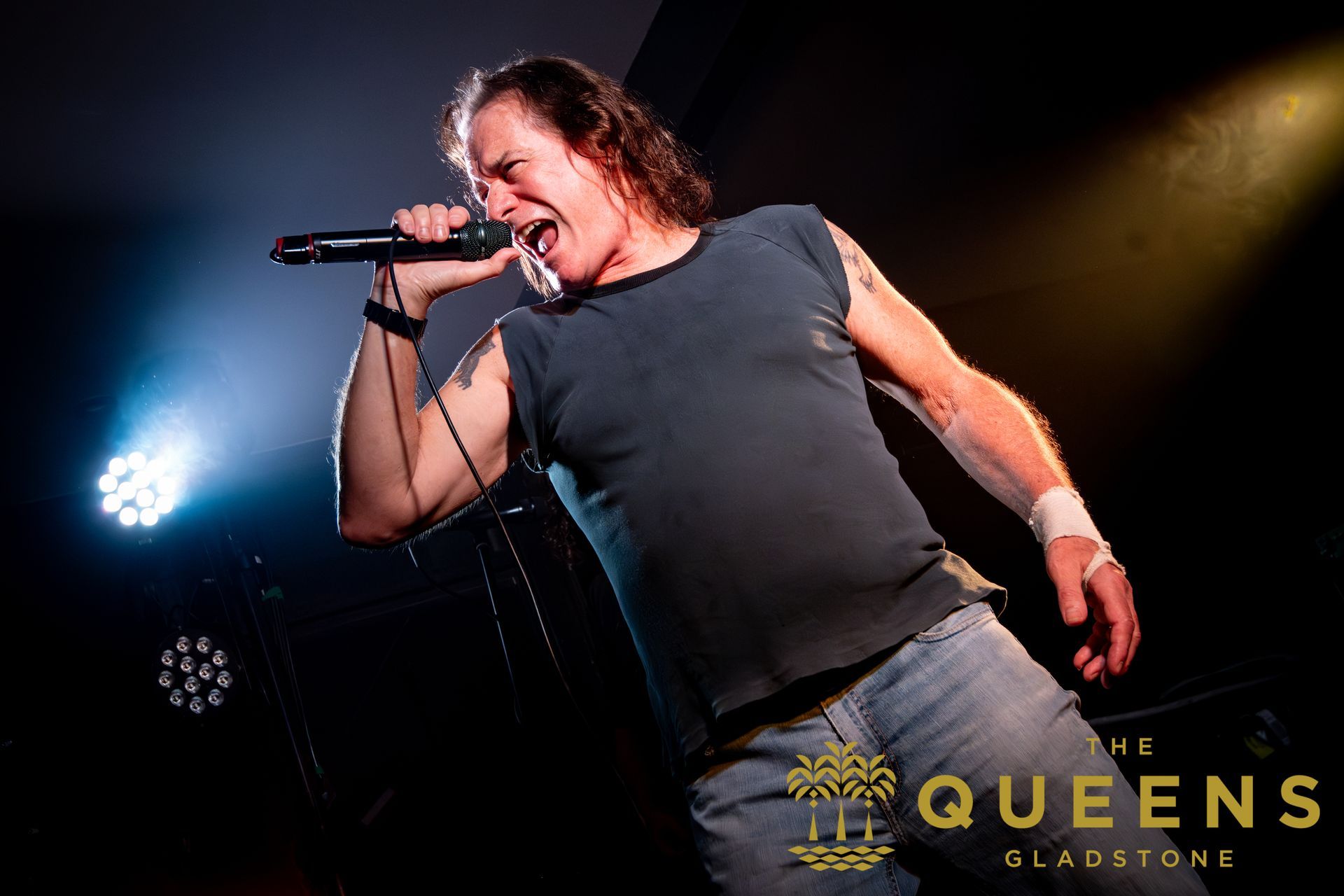 Singer belting into a microphone onstage under dramatic blue and yellow lights