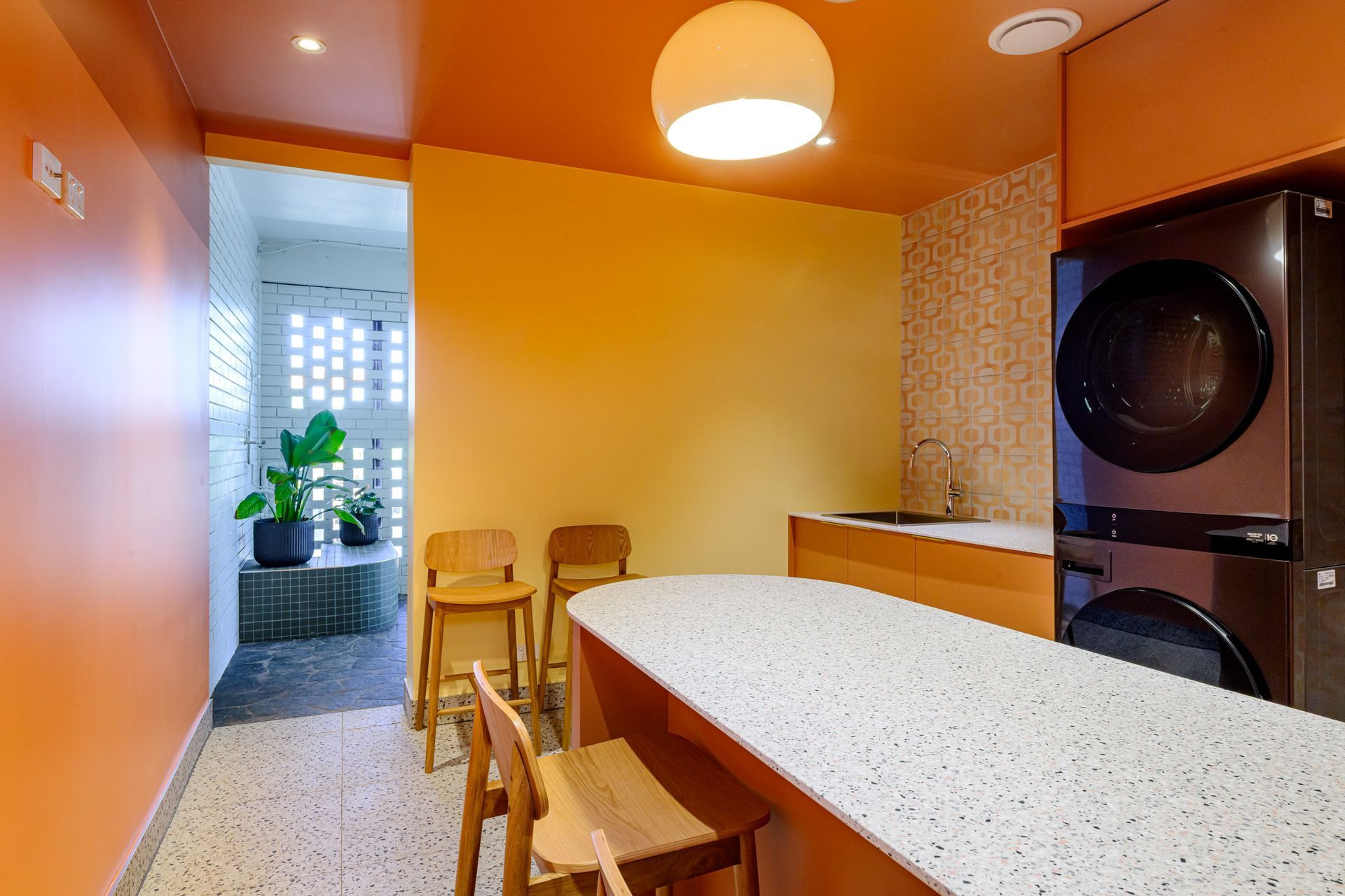 Orange kitchen with white countertop, wooden stools, and black appliances beside a small dining nook.