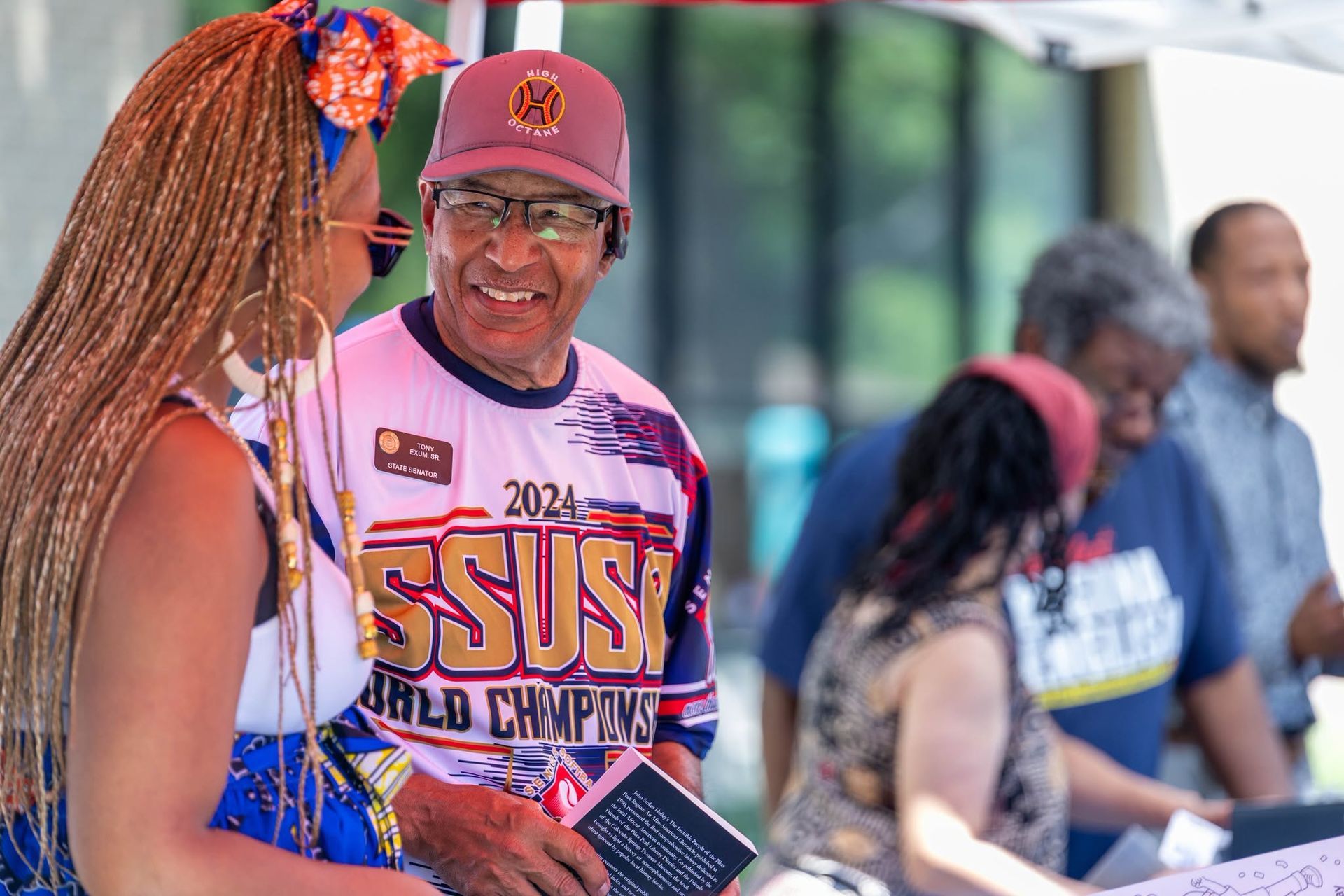 Two people chatting at an outdoor event, one wearing a purple SSU championship shirt and cap