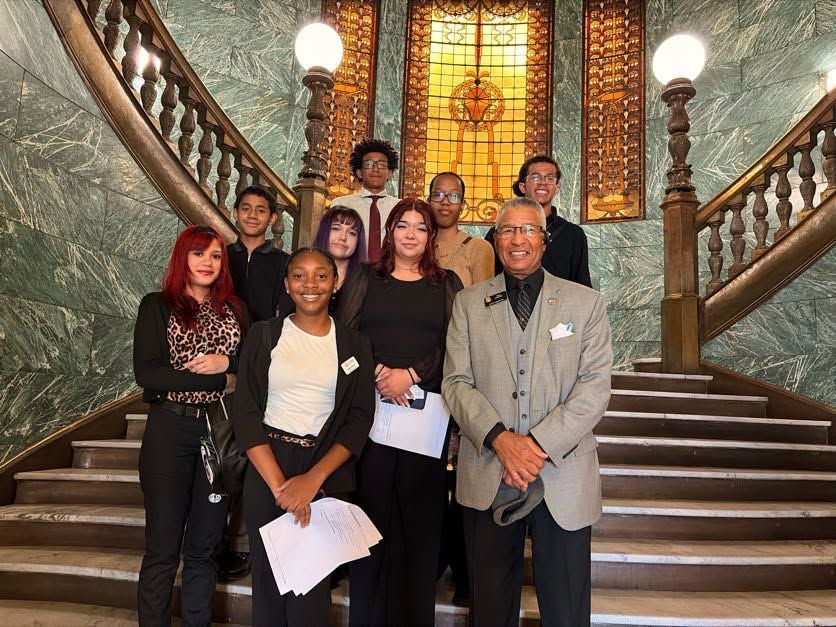Group of people posing on a grand staircase in front of stained glass windows.