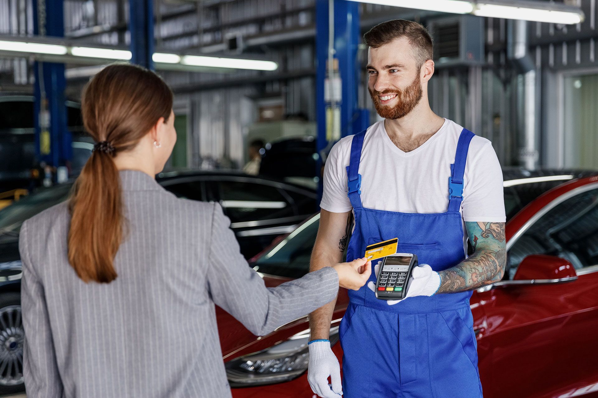 A woman is giving a credit card to a mechanic in a garage.