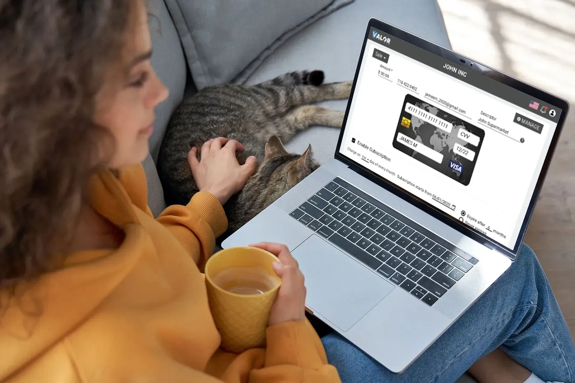 A woman is sitting on a couch with a laptop and a cup of coffee.