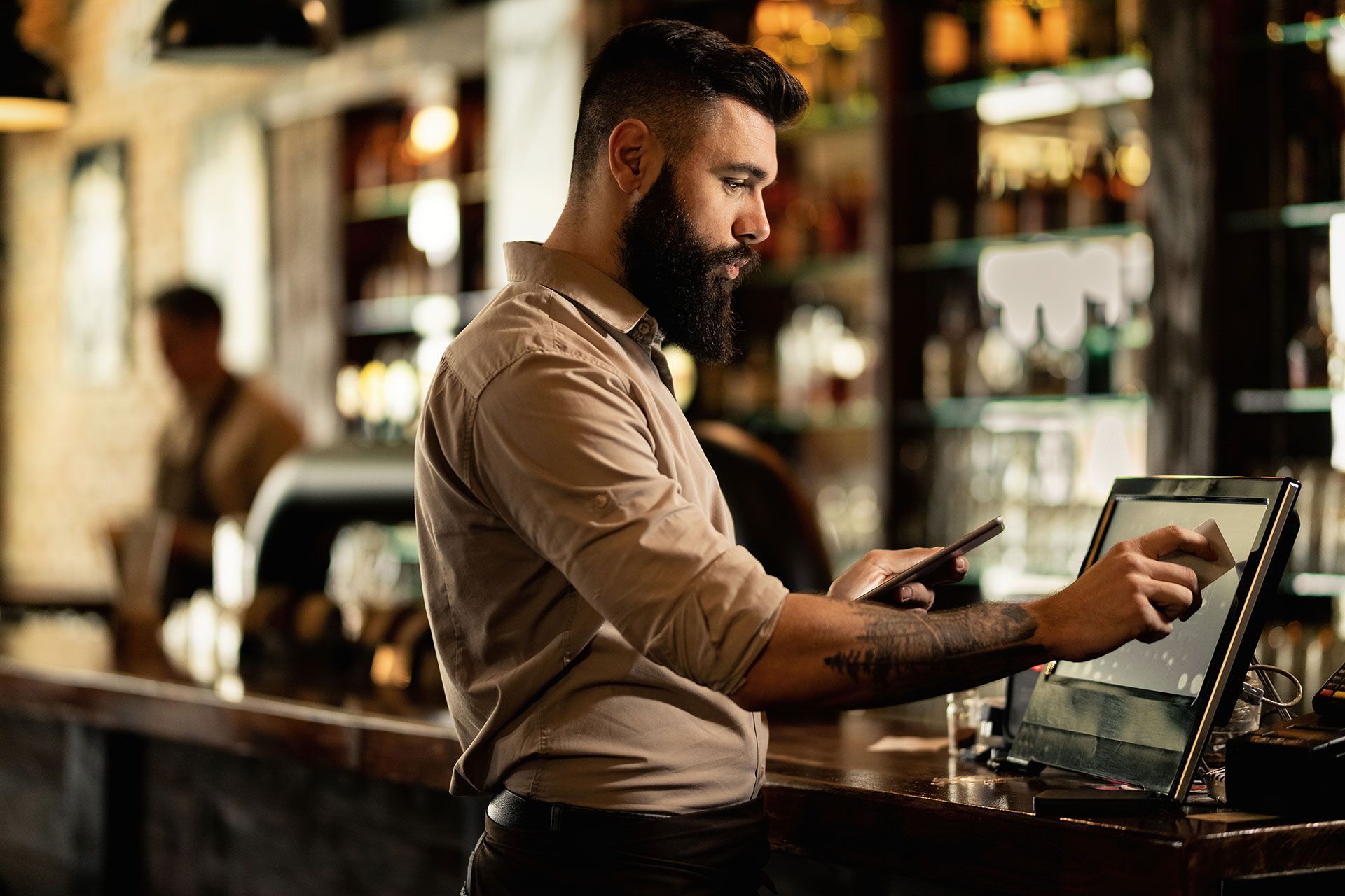 A man with a beard is sitting at a bar using a tablet computer.